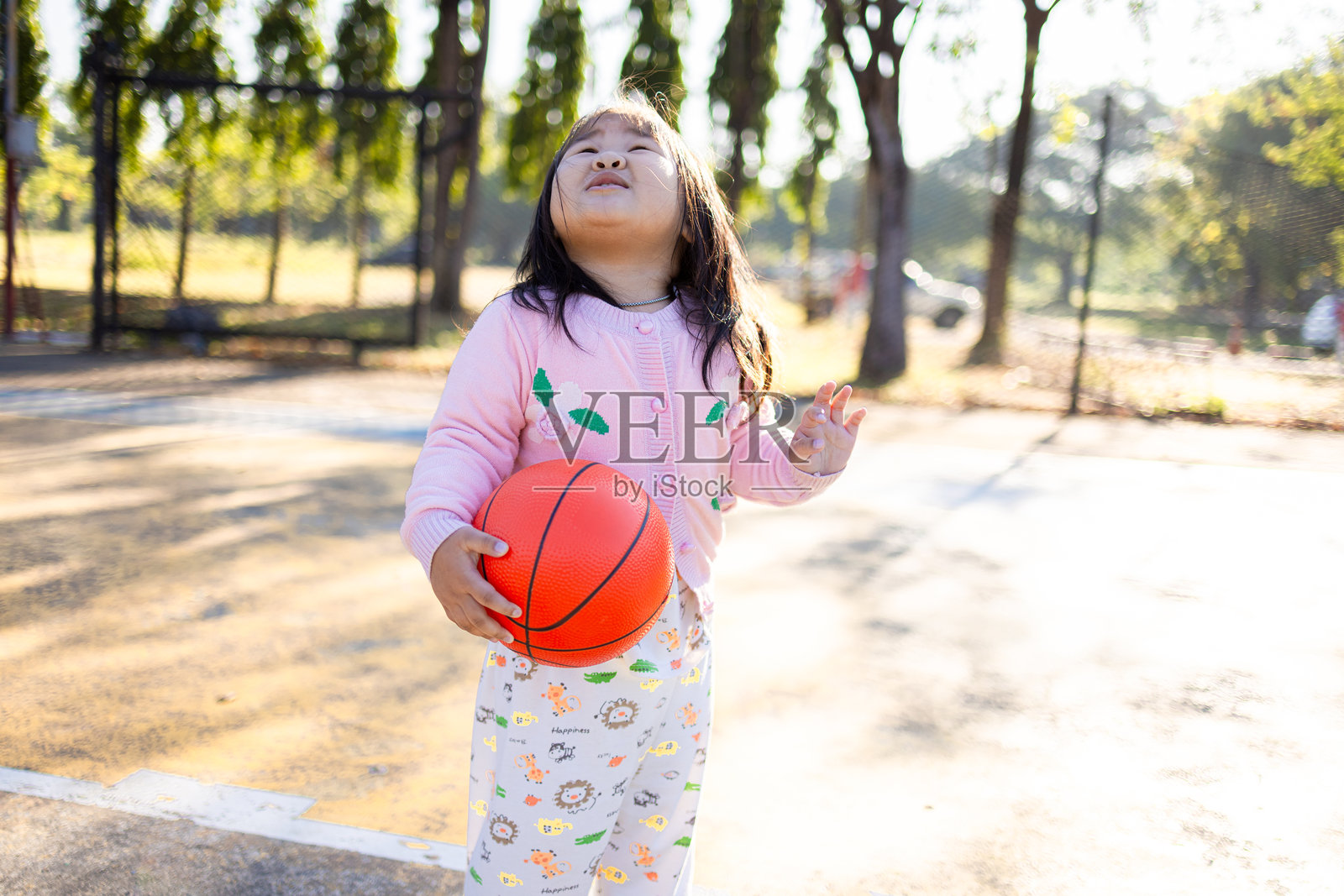 小女孩拿着篮球，在户外球场上抬头望着篮筐。照片摄影图片