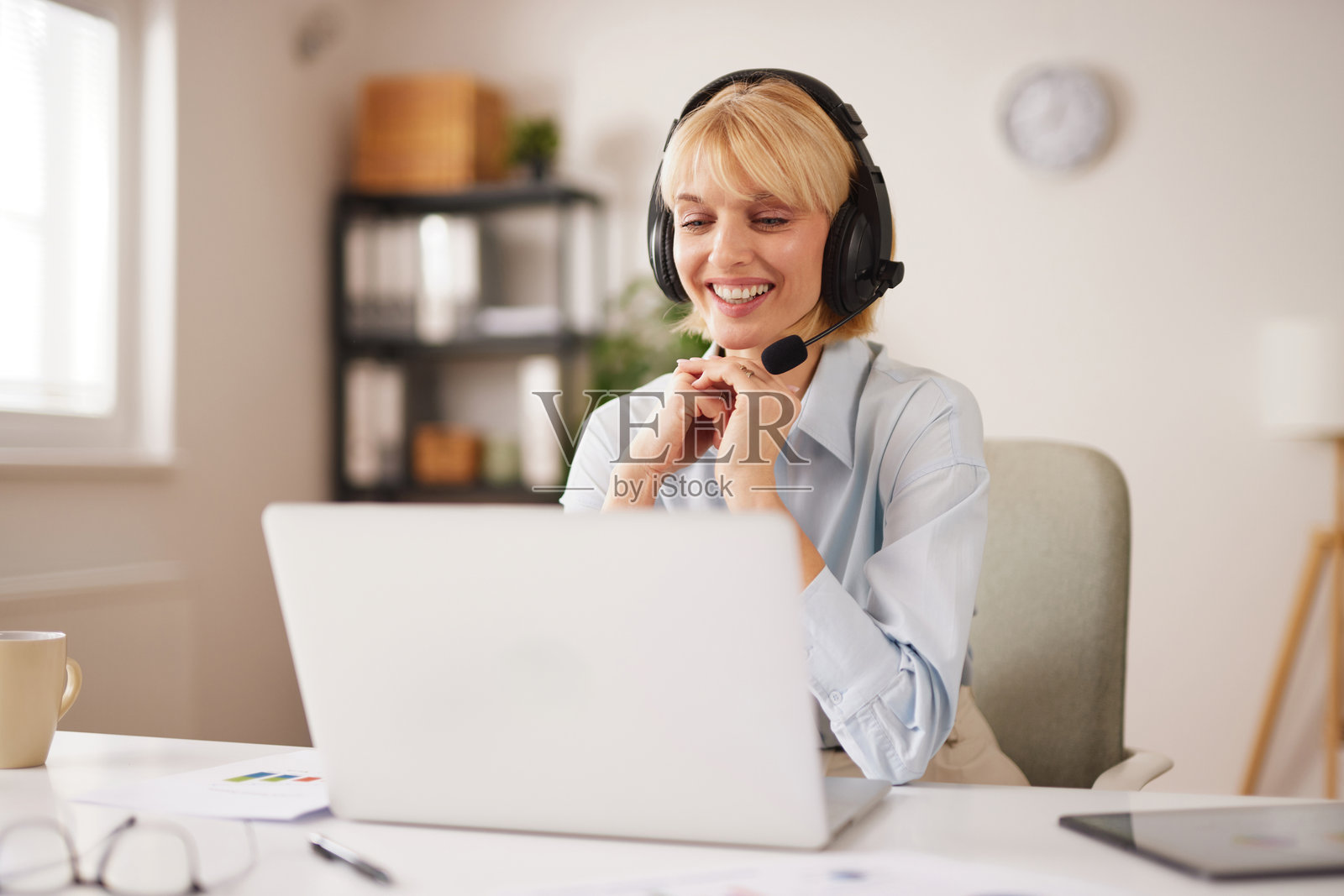 一位客户服务代表在明亮的办公室里，一边使用笔记本电脑工作，一边与客户沟通。照片摄影图片