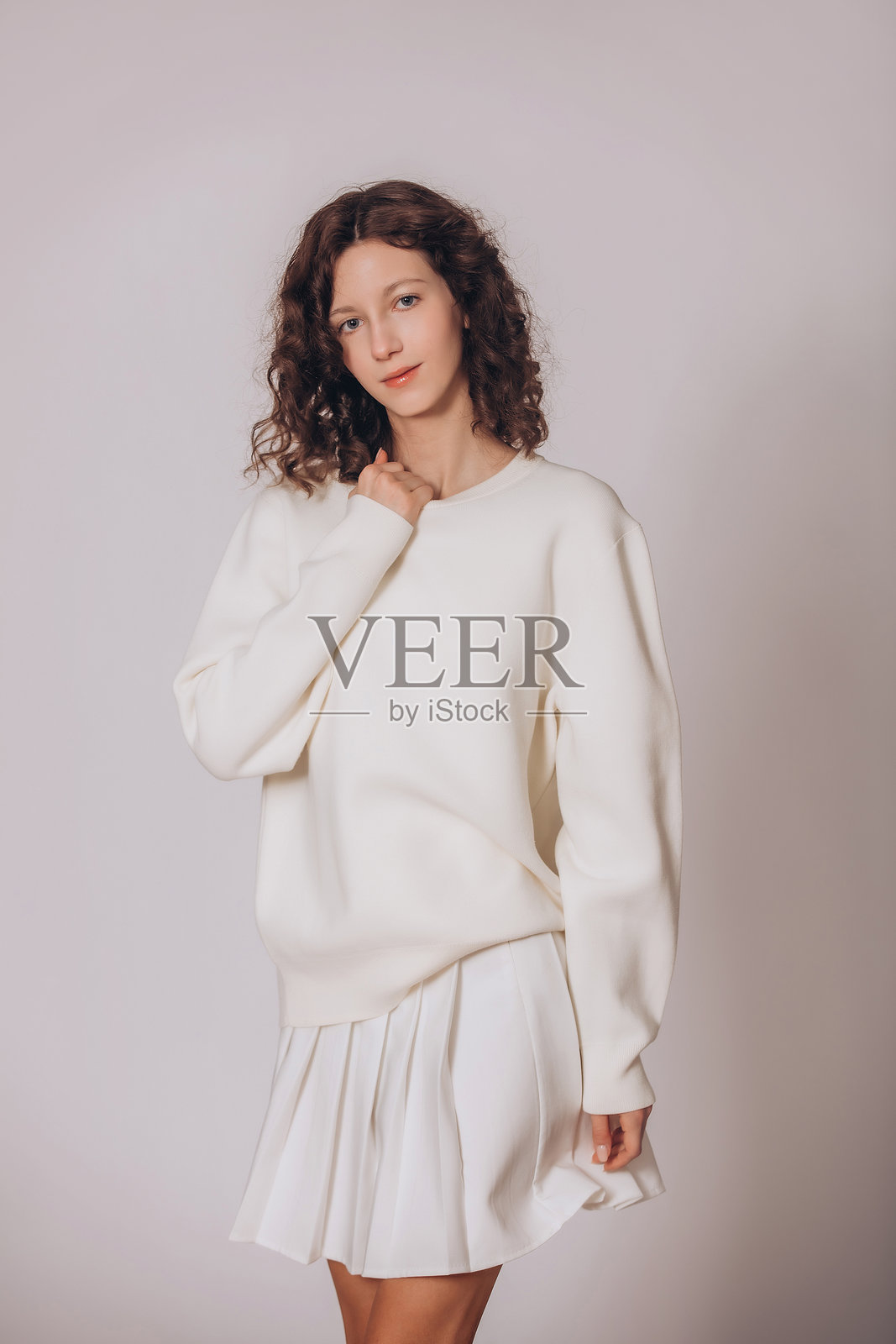 一位年轻美丽的棕发卷发女孩，身穿白色运动衫，背景为白色照片摄影图片