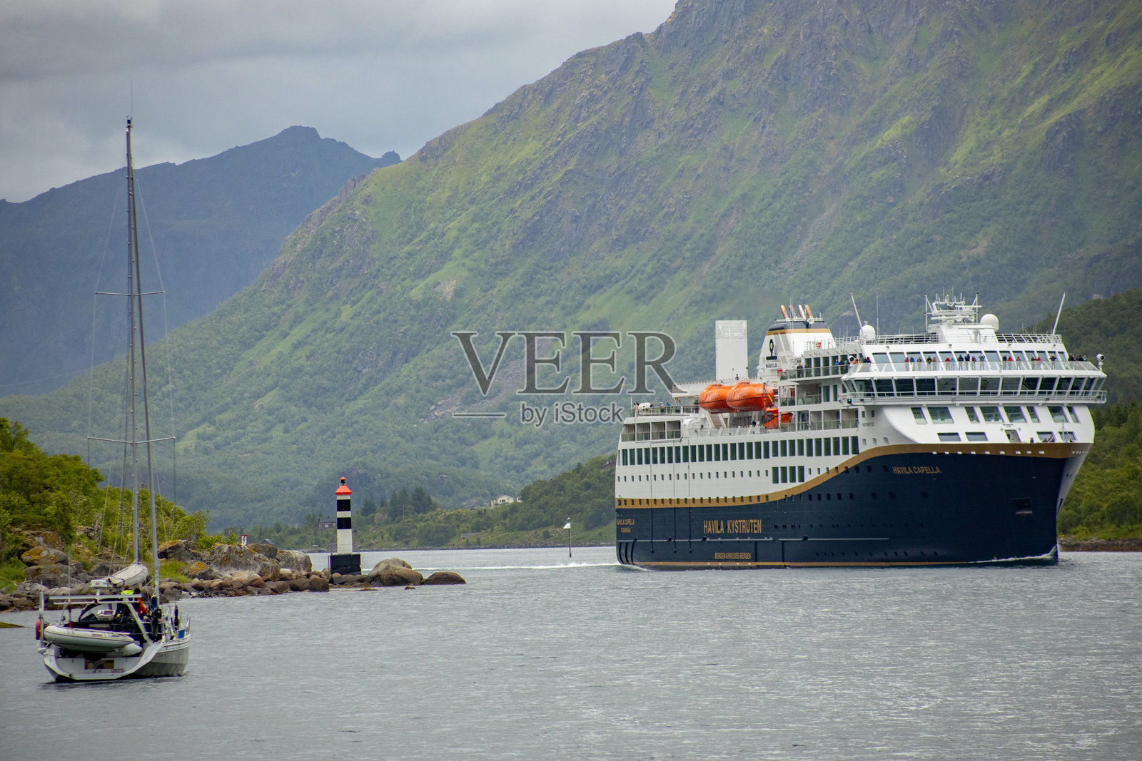 一艘小型帆船在挪威罗弗敦峡湾等待邮轮驶过照片摄影图片