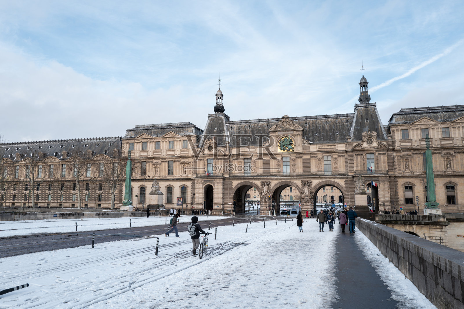 人们走在通往法国巴黎卢浮宫的雪桥上，也有人在桥上骑行。照片摄影图片