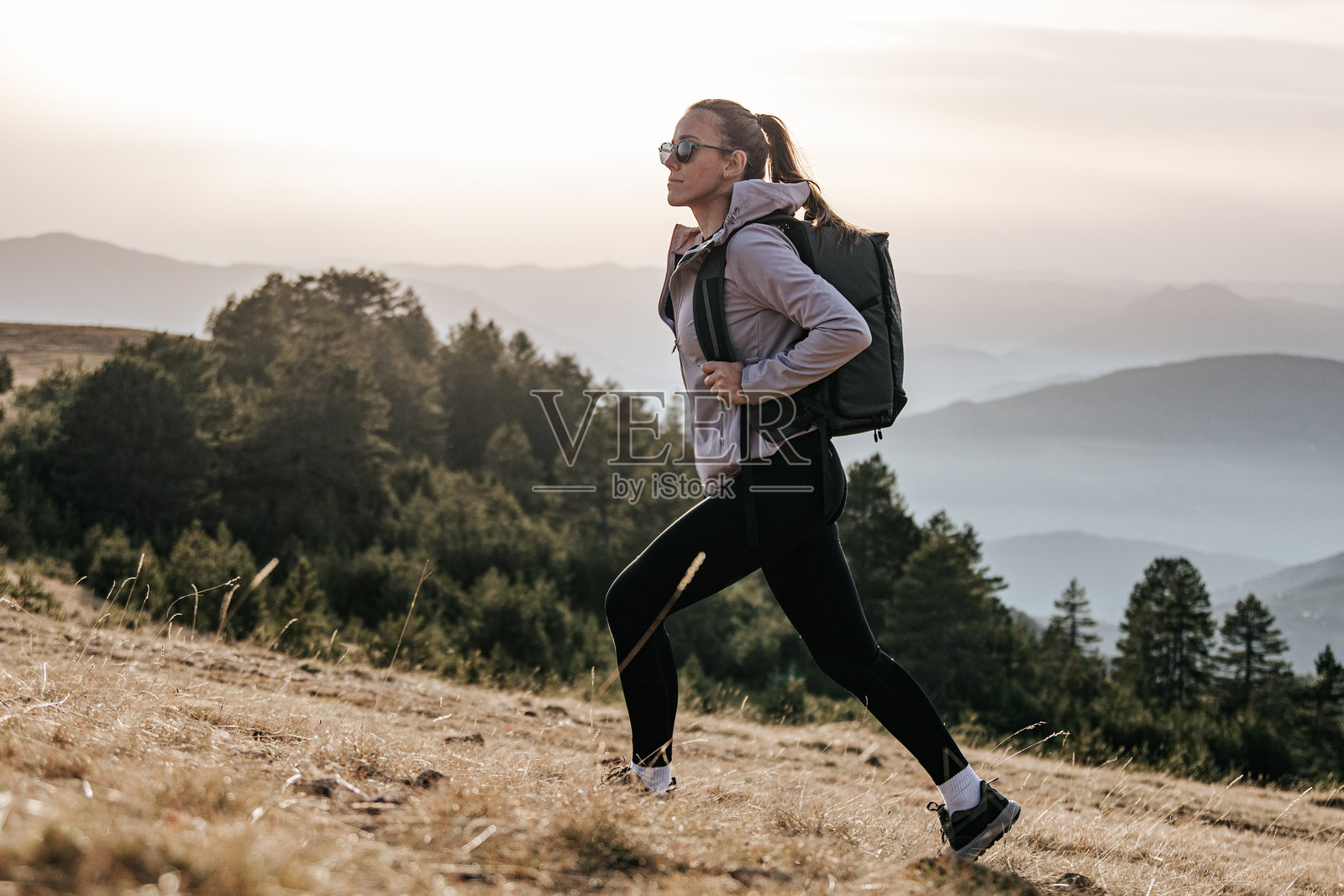 日出时，一位背着背包的活力女性在山间徒步照片摄影图片