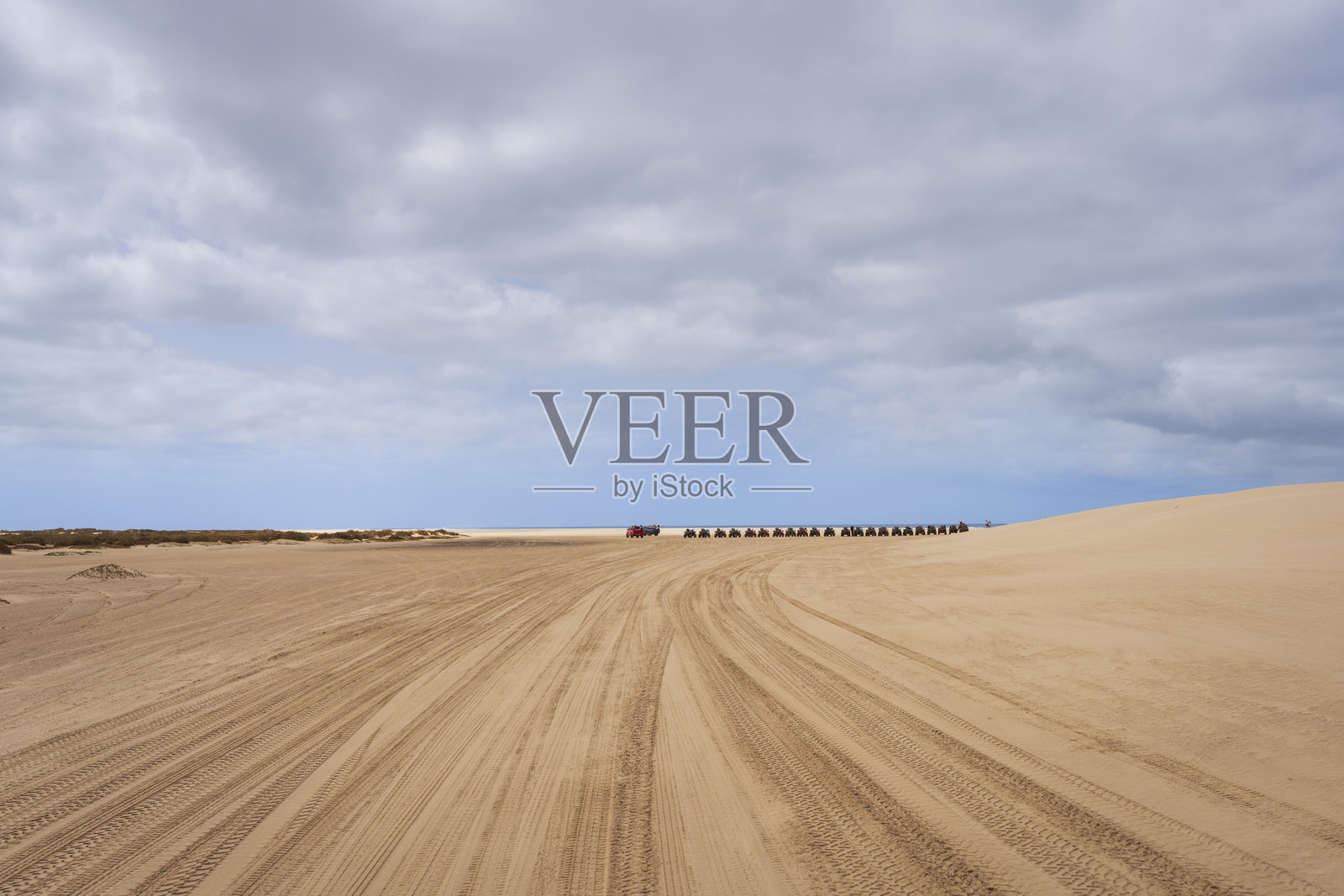 远处沙漠中的一群四轮摩托车在多云天气下排成一列照片摄影图片