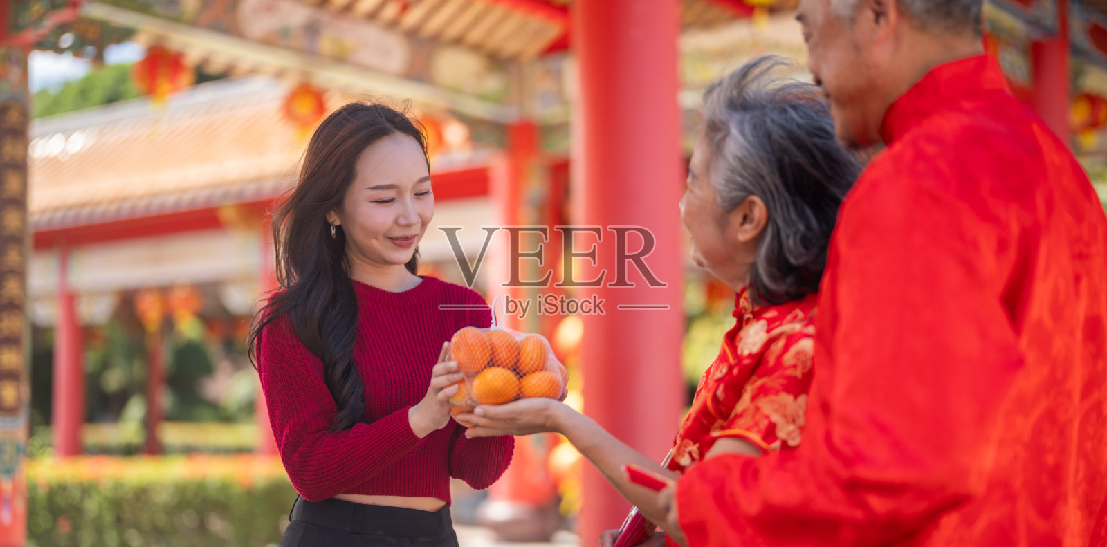 快乐的亚裔女儿在中国寺庙给年迈的父母送橘子，家人庆祝农历新年，体现孝道、尊敬、好运和传统节日概念照片摄影图片