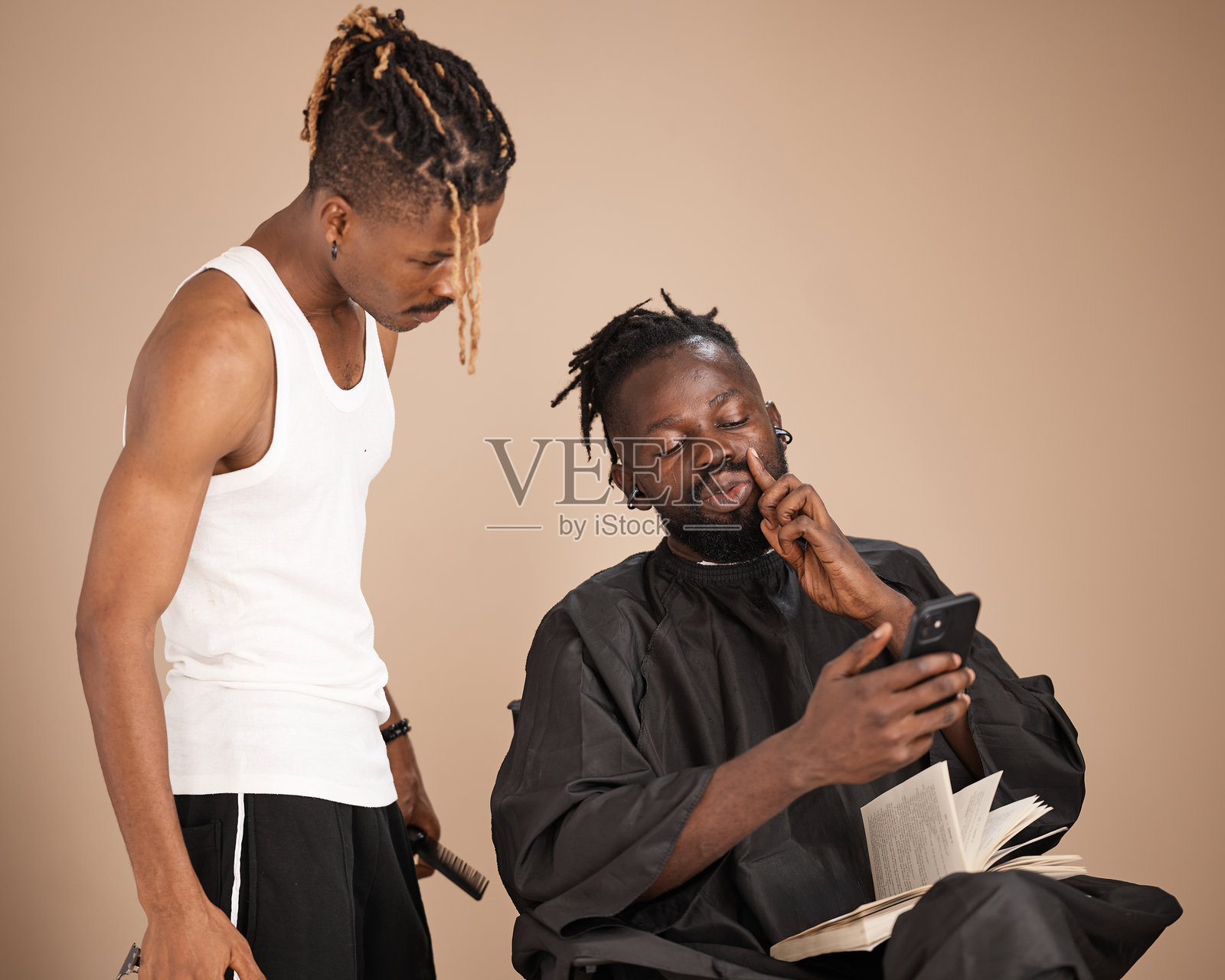 年轻的尼日利亚理发师和顾客在理发时一起看手机照片摄影图片