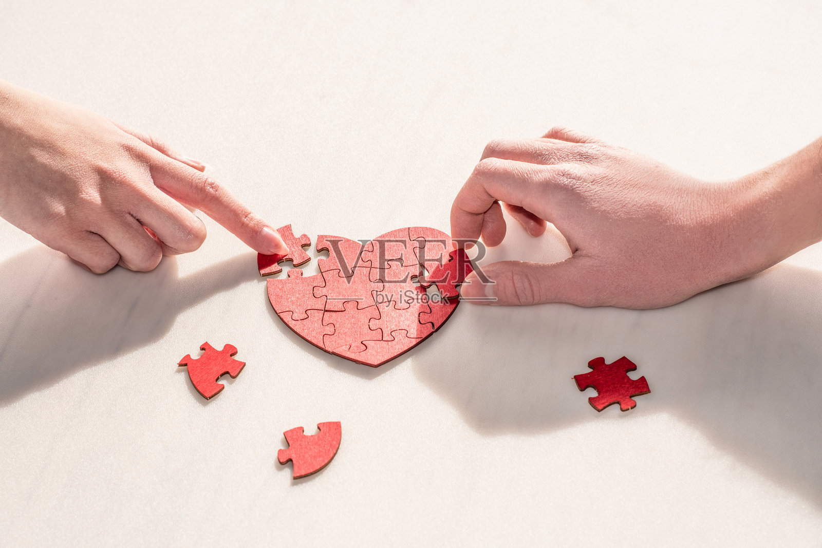 男女双手合作，用拼图碎片组成一个心形照片摄影图片