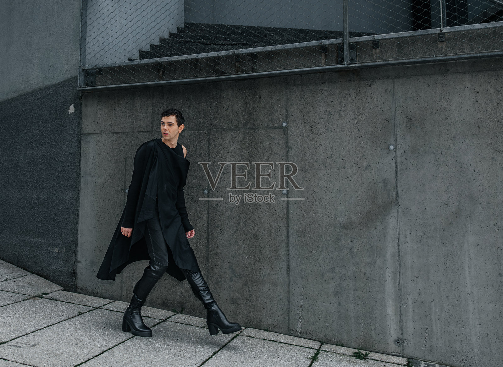 身穿时尚黑色服装的亚洲年轻女性走过水泥墙照片摄影图片