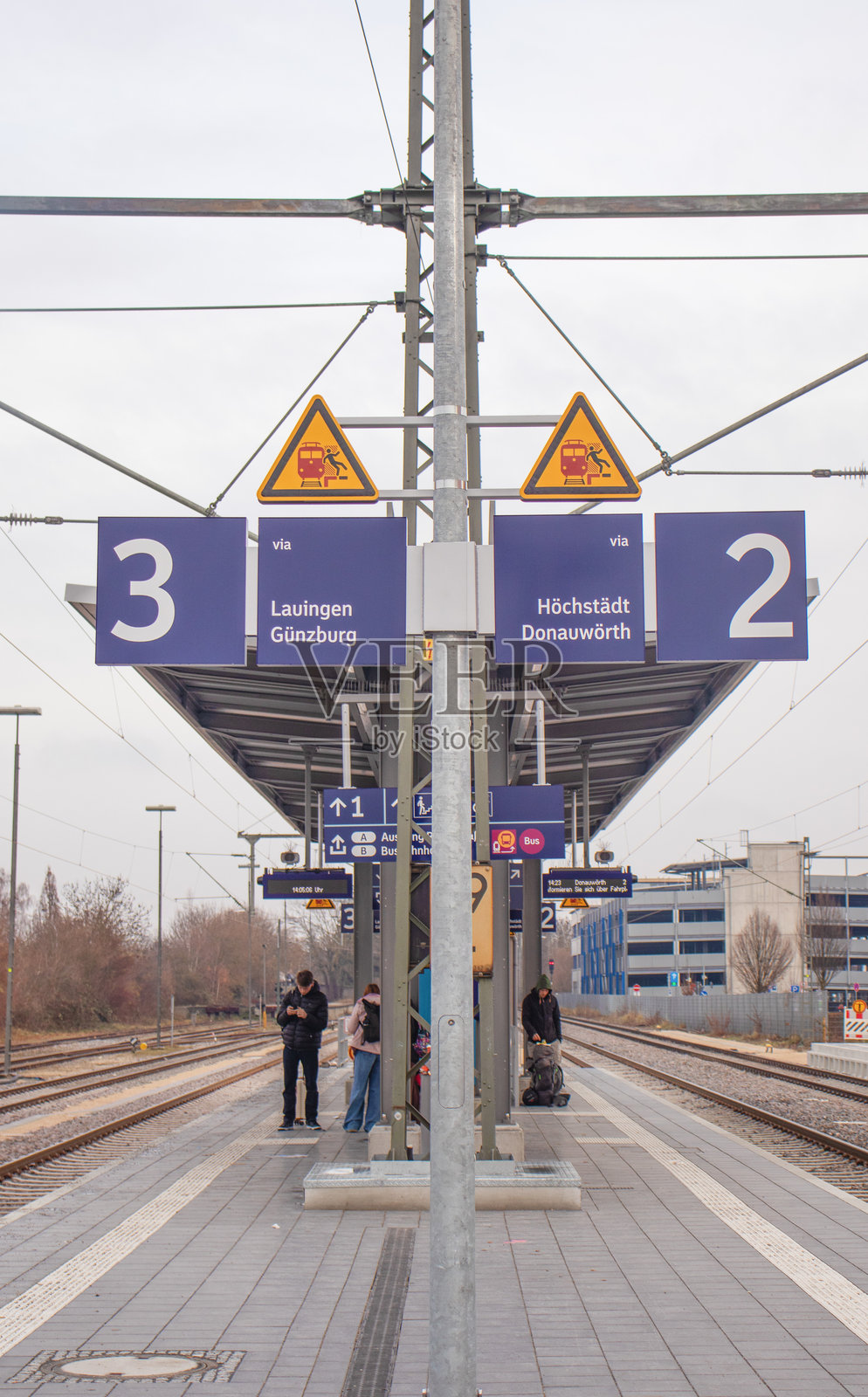 2025年11月30日,在德国巴伐利亚州迪林根火车站,一个阴天的站台上,有指示牌、警告标志,以及等待的乘客。照片摄影图片