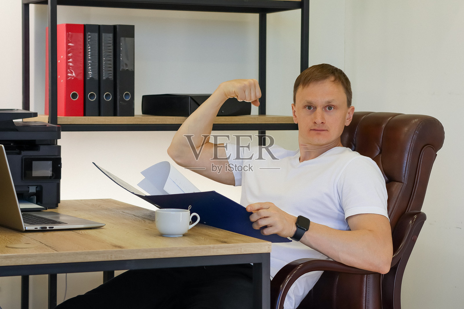 男人在办公室里展示肱二头肌，手中拿着文件夹照片摄影图片