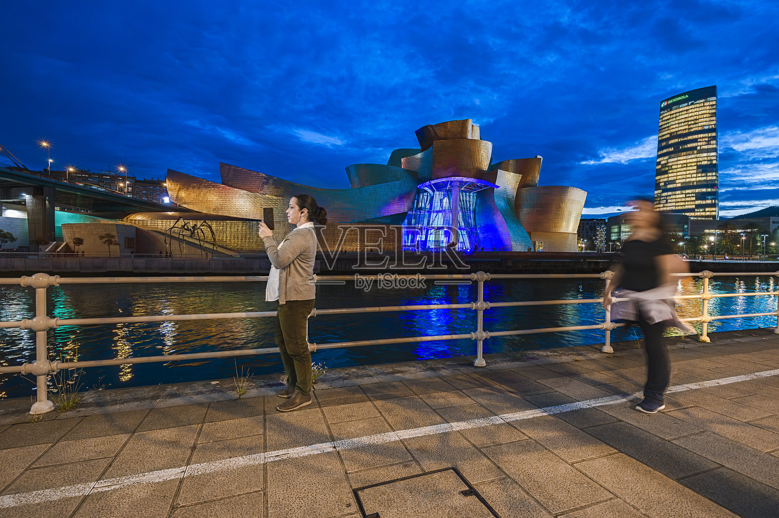 游客在蓝色时刻于河边拍摄毕尔巴鄂古根海姆博物馆照片摄影图片