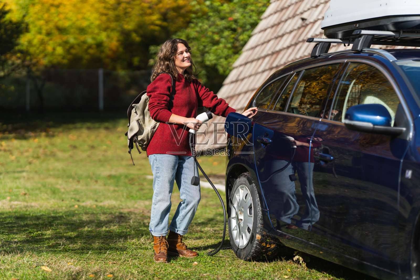 背着背包的女性旅行者和充电中的电动汽车照片摄影图片