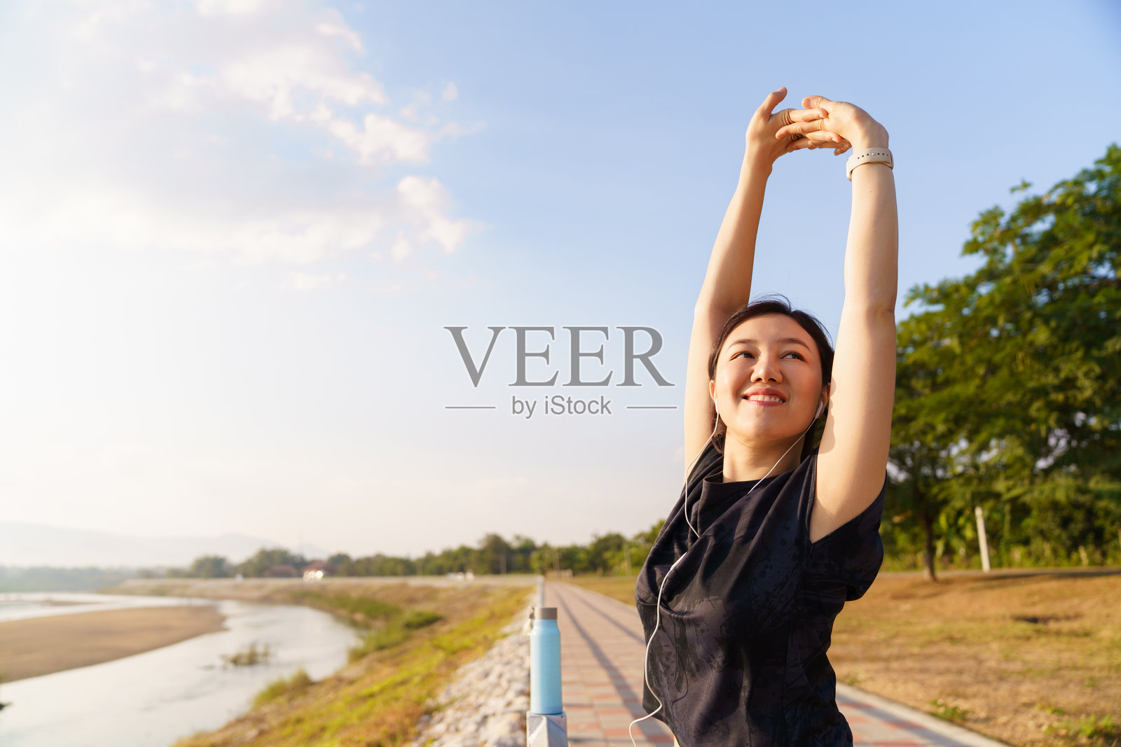 一位女性在河边户外运动后伸展手臂。健身恢复与健康意识概念。照片摄影图片