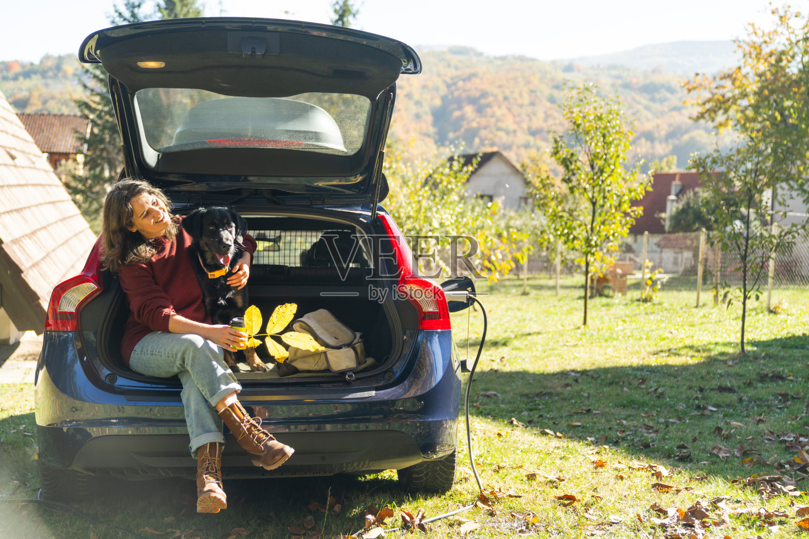 女士和她的狗一起进入电动汽车的后备箱照片摄影图片