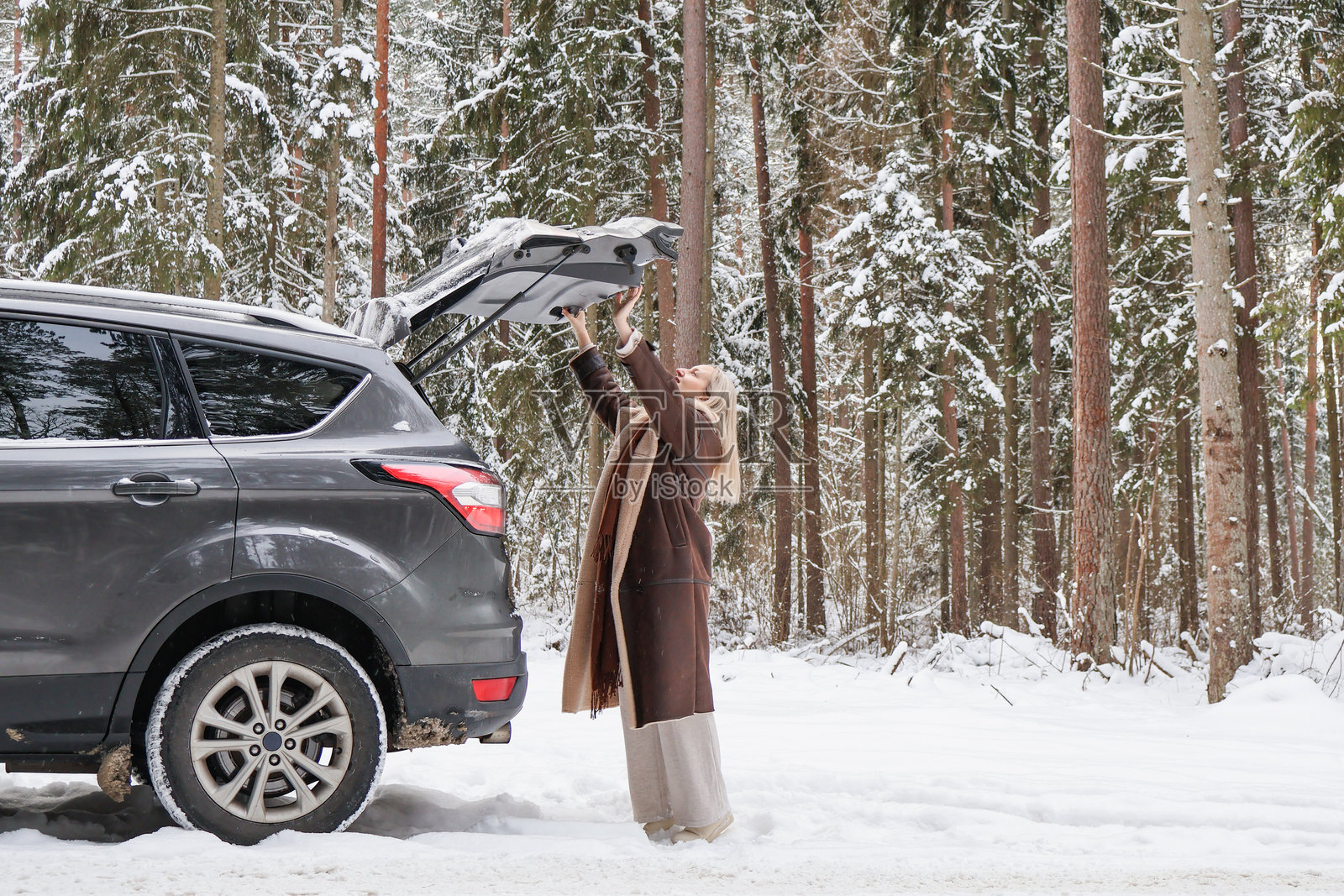 一位中年女子穿着暖和的外套，在雪林中打开SUV的后备箱。照片摄影图片