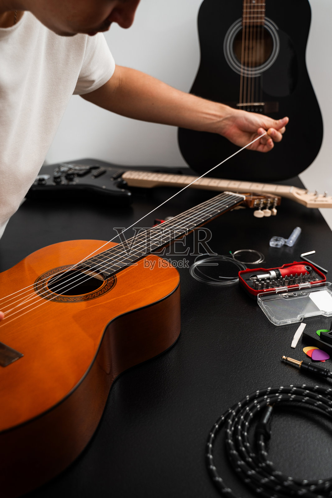 正在为原声吉他更换新琴弦，吉他手正在将新琴弦安装到指板上。照片摄影图片