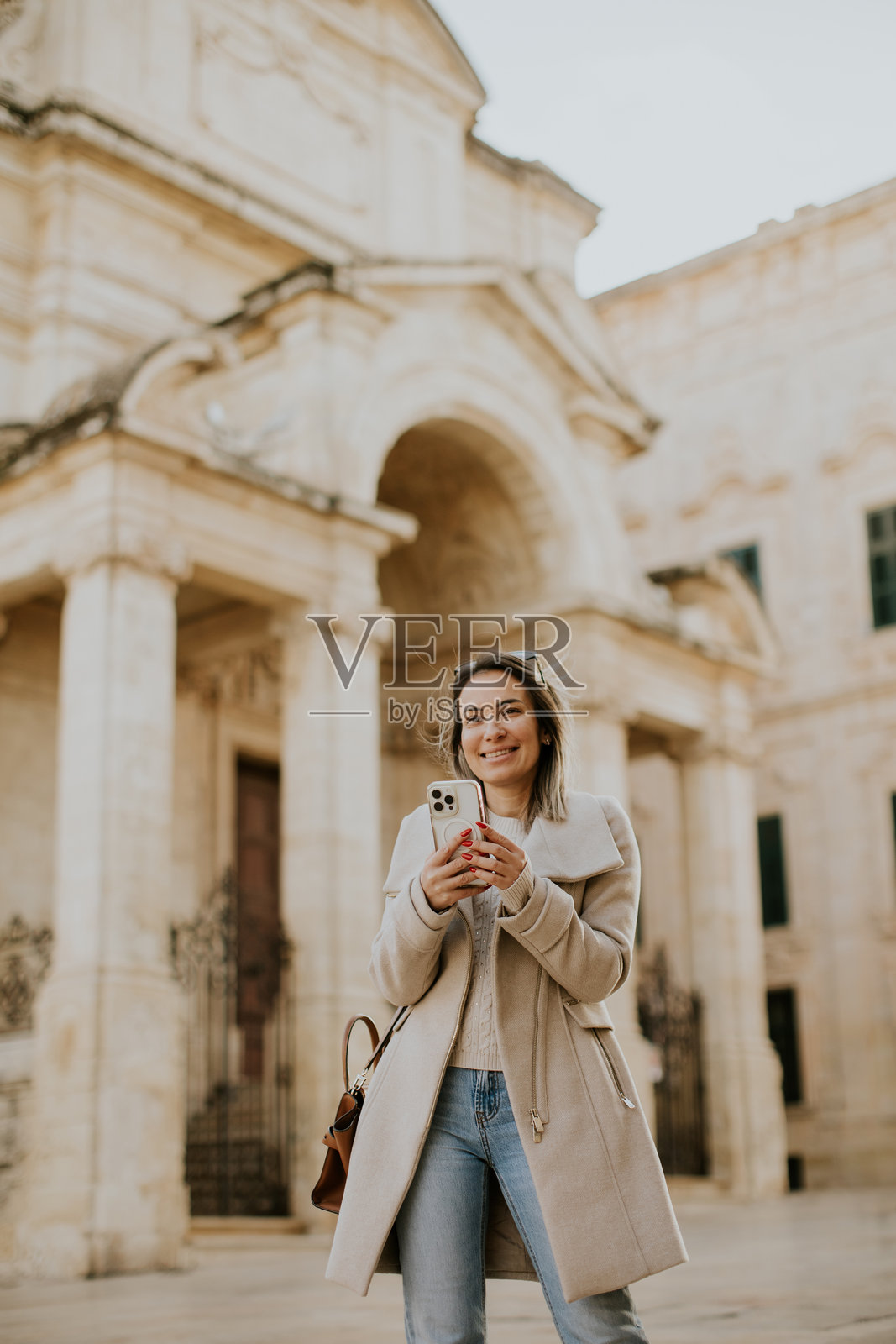 女子在明亮的马耳他历史古城街道上边走边使用手机照片摄影图片