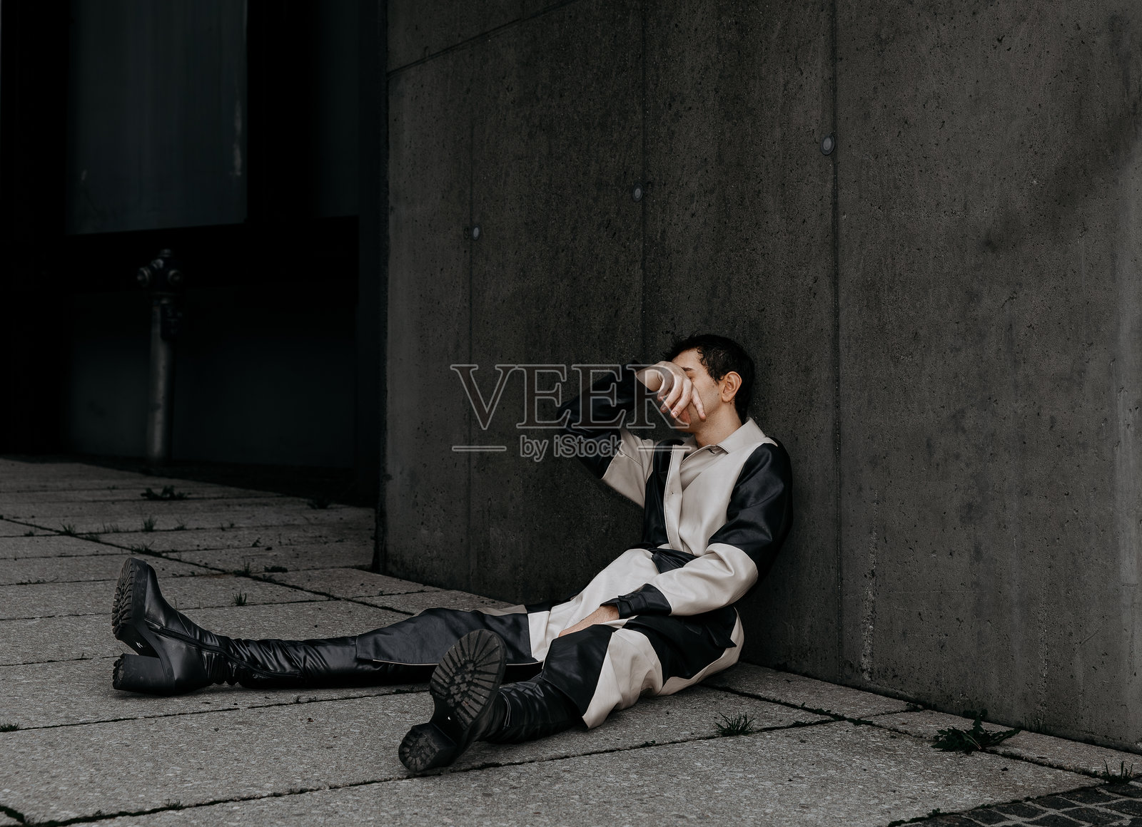 一个年轻男子坐在人行道上，遮住脸，穿着黑白相间的衣服照片摄影图片