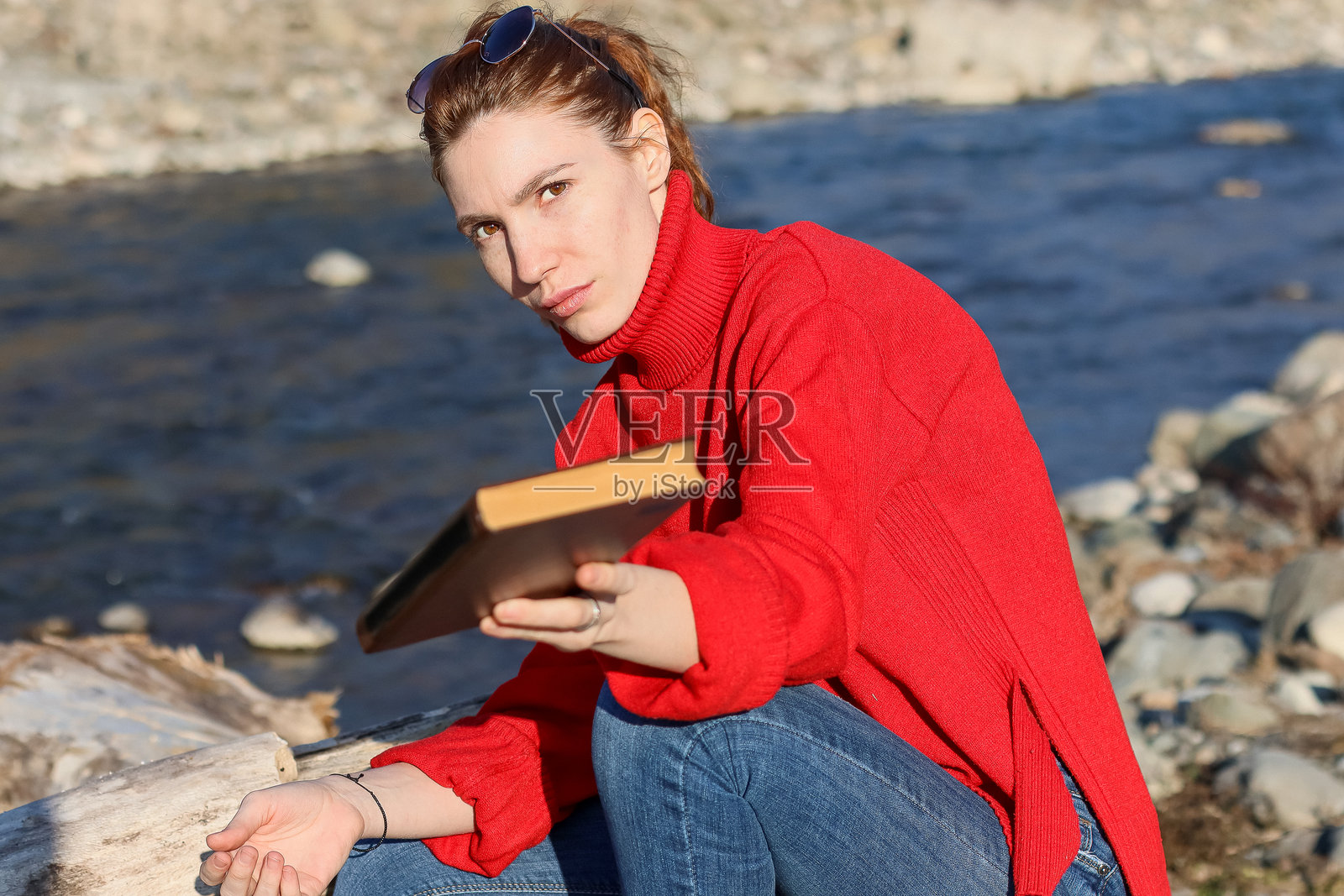 一位女士坐在河边，将书本递向观者照片摄影图片