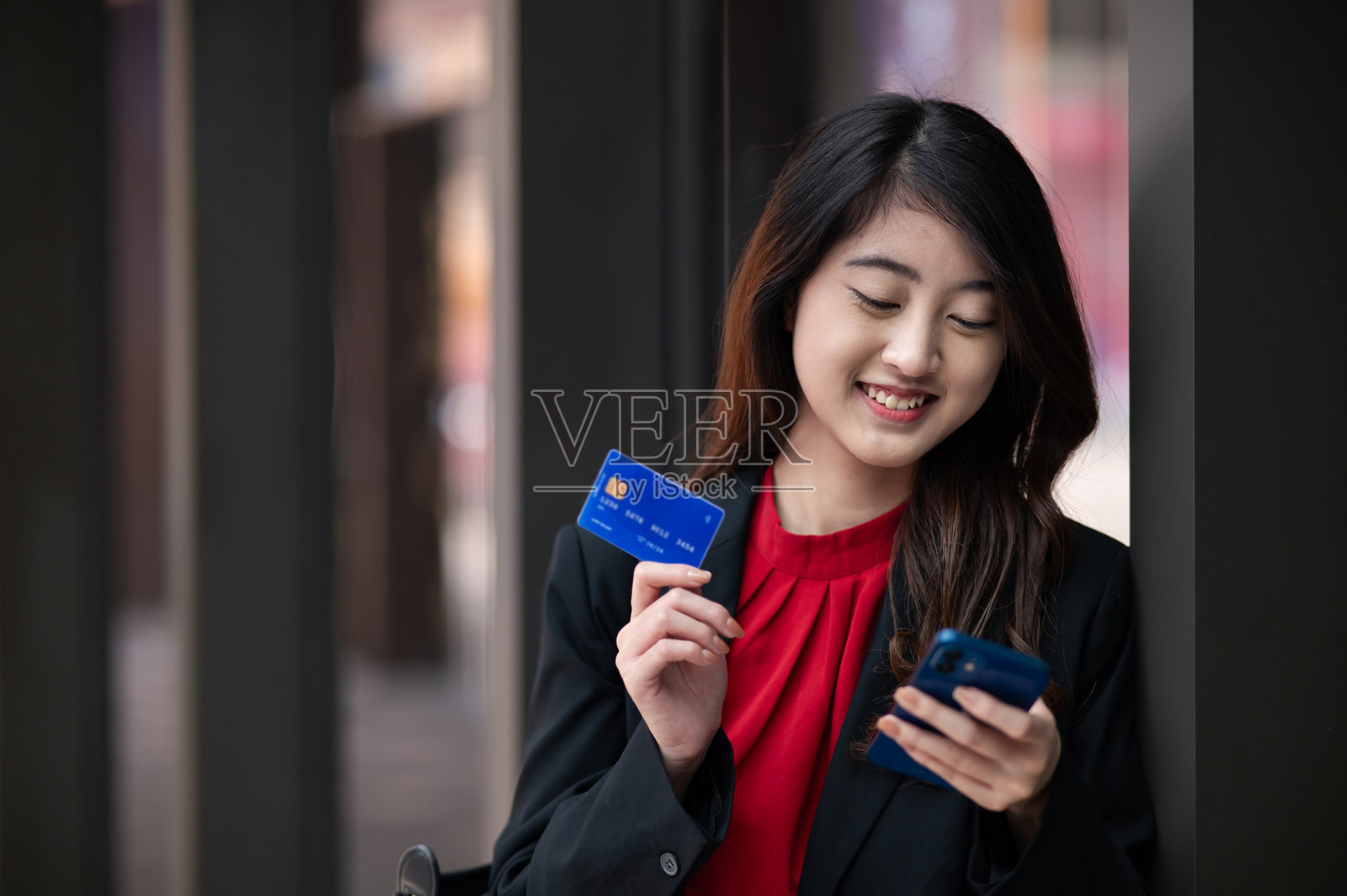 一位年轻的亚洲女商人，在现代办公室里手持信用卡和智能手机照片摄影图片