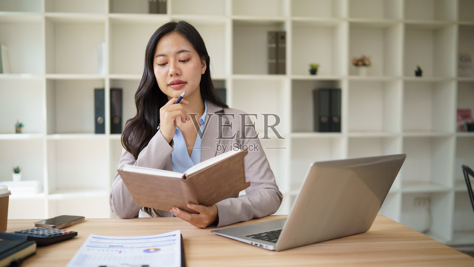 一位沉思的女商人在现代办公桌前阅读笔记本并规划任务。照片摄影图片