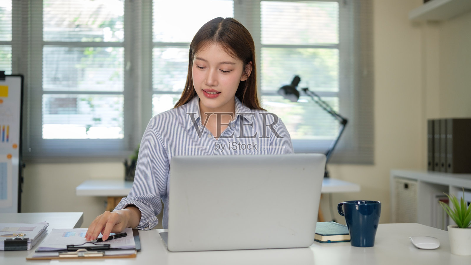 年轻的女商人正在用笔记本电脑和财务文件在办公桌前工作，分析数据。照片摄影图片