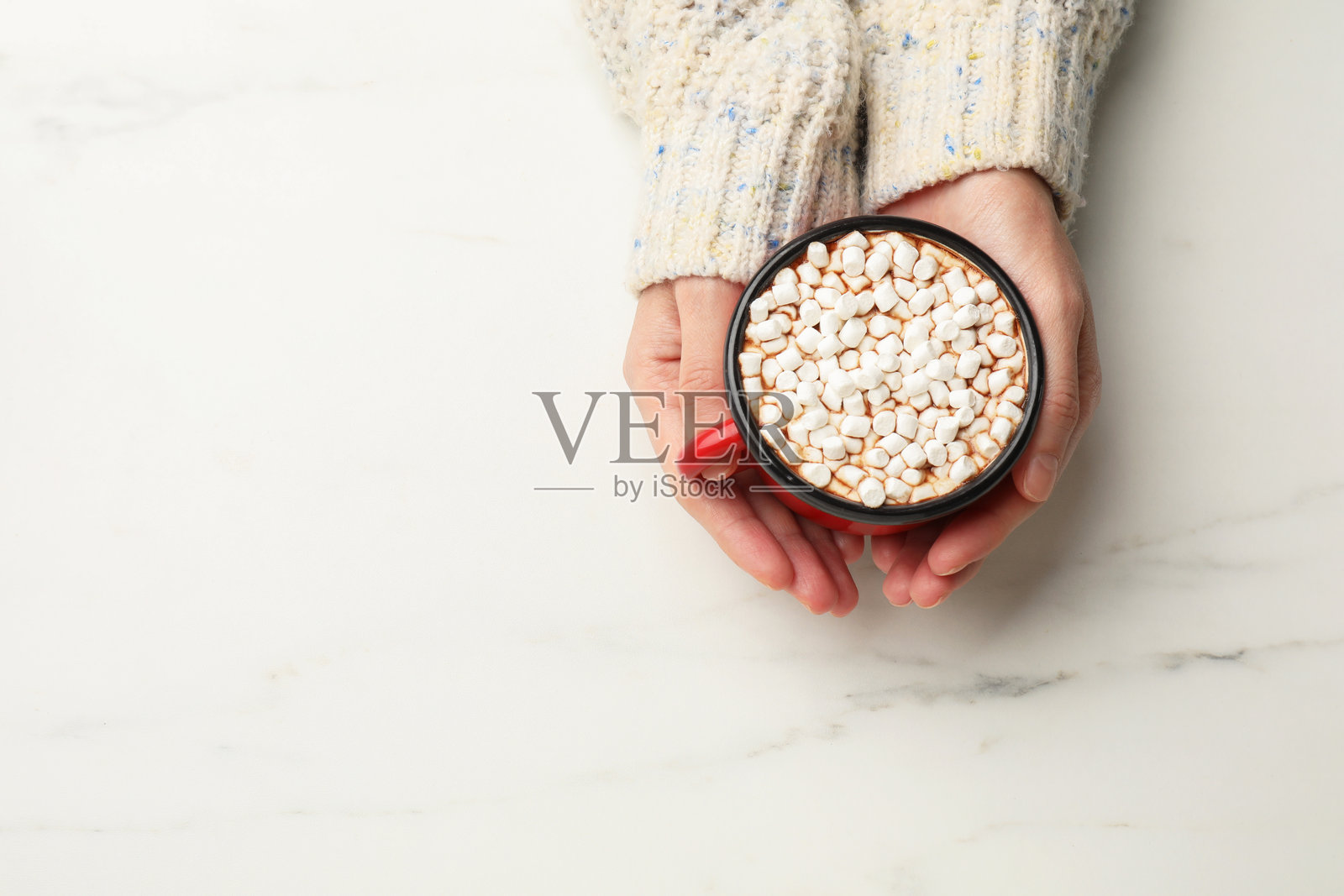 女人在白色大理石桌旁享用一杯美味的热巧克力和棉花糖，俯视视角，留有文字空间。照片摄影图片