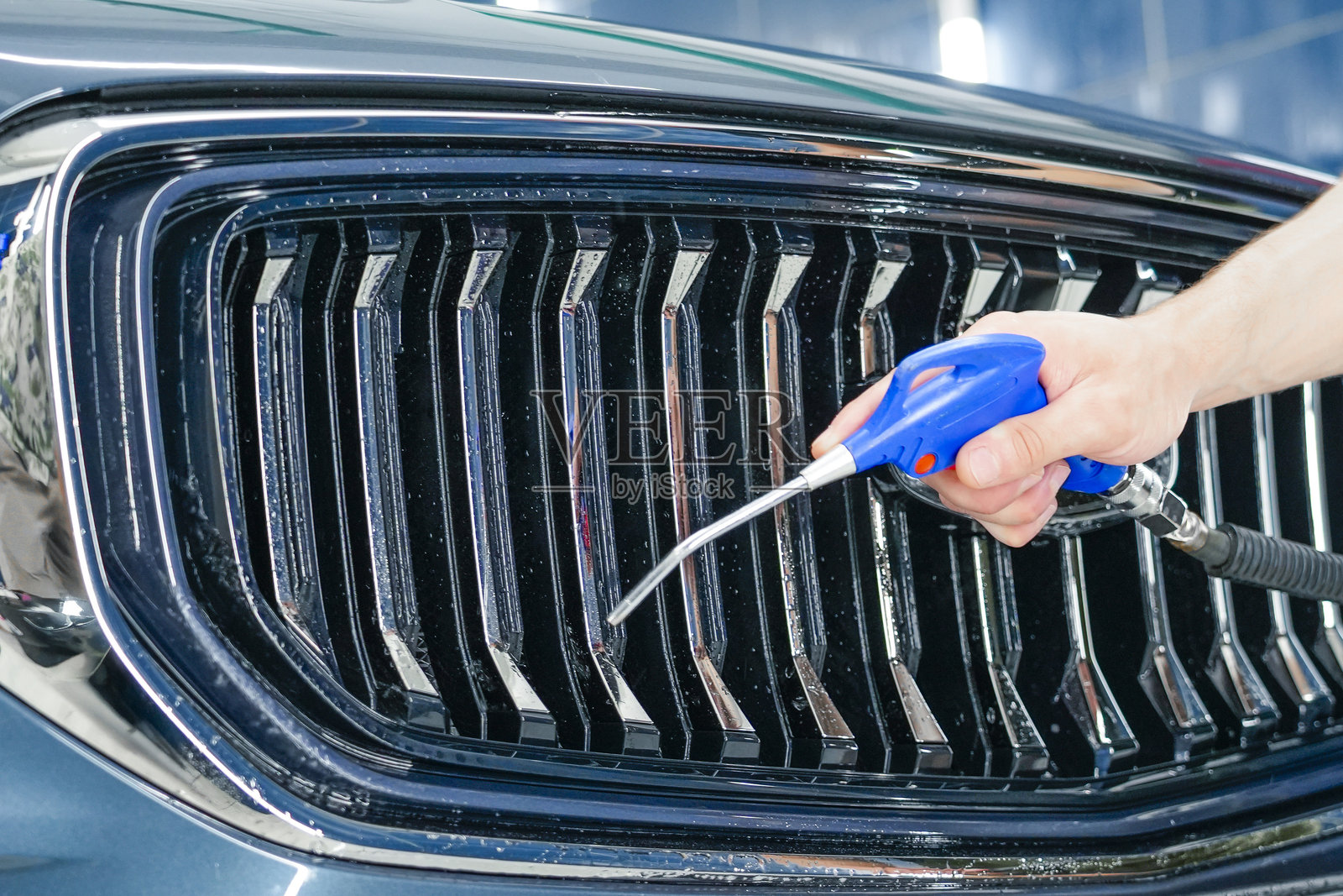 一位汽车美容师正在车库里使用气枪清理一辆现代汽车的前格栅区域，他专注于实现精准的清洁效果。照片摄影图片