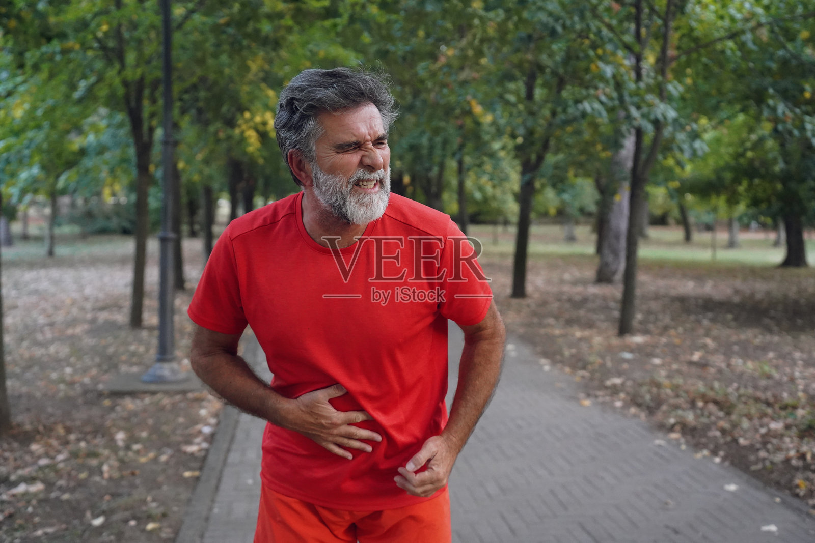 年长的男性在公园锻炼后感到胃部不适照片摄影图片