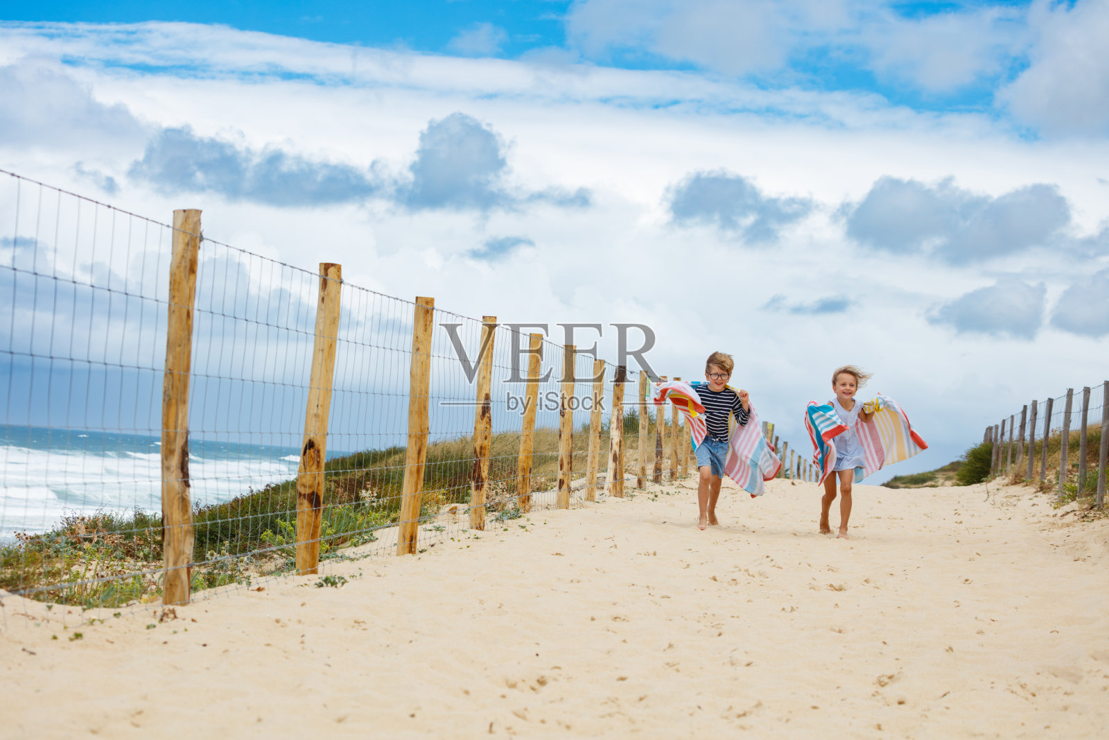 孩子们在沙滩小径上开心地奔跑，带着毛巾照片摄影图片