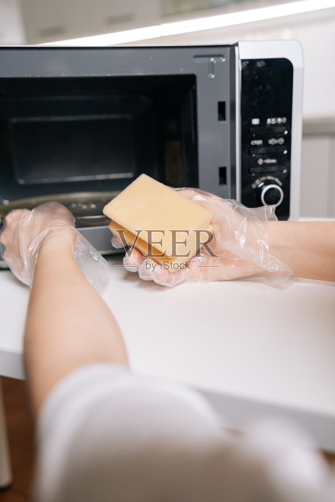 女性戴着一次性手套，用黄色海绵清洁微波炉内部，保持厨房卫生标准和家庭清洁，俯视特写照片摄影图片