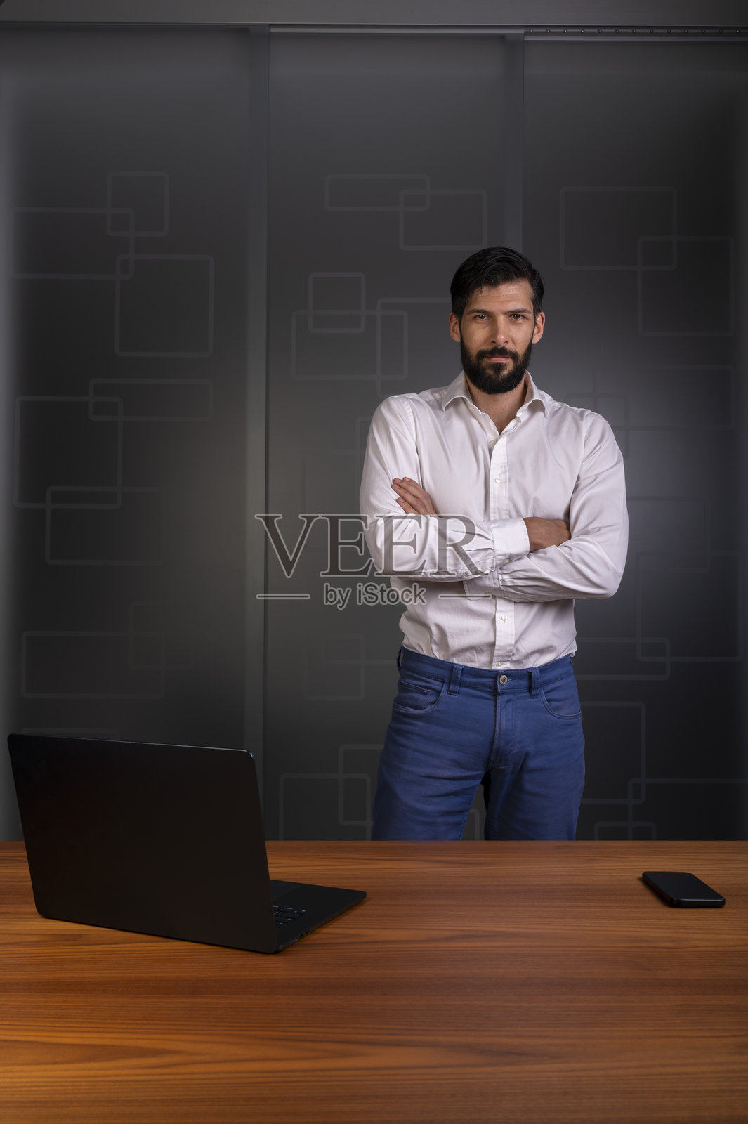 身穿白衬衫和蓝色裤子的男士站在现代办公室，代表公司或企业。照片摄影图片