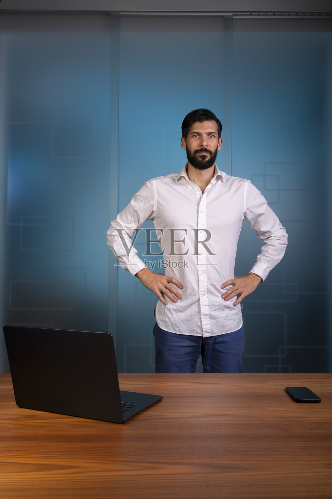 身穿白衬衫和蓝色长裤的男士站在现代办公室，代表公司或企业照片摄影图片