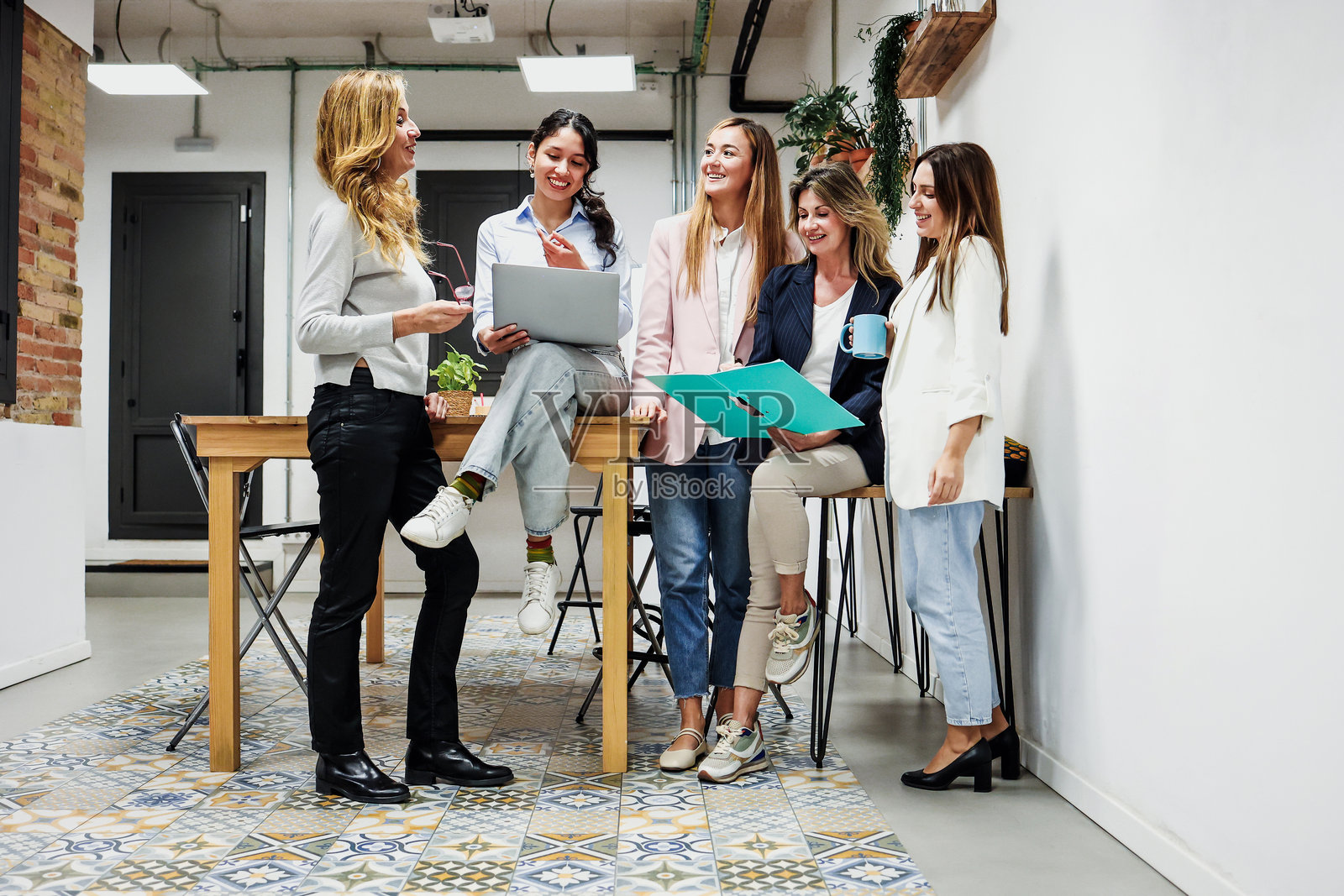 不同年龄段的成功西班牙裔女性商务人士在办公室协作，使用笔记本电脑工作。这是一个多元化的、不同族裔的女性创业者和跨代际团队在工作场所分享想法的场景。照片摄影图片