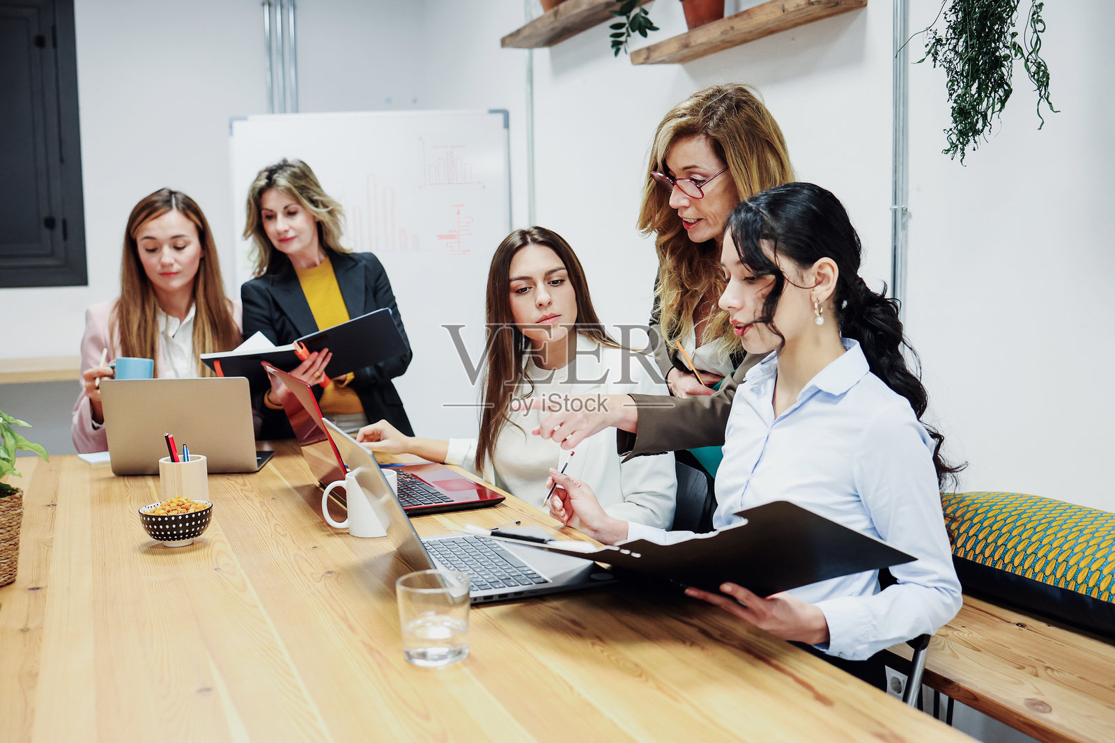 不同年龄段的成功西班牙裔女性团队在办公室合作并使用笔记本电脑。多元化、多民族的女性企业家和多代人组成的团队在工作场所分享创意。照片摄影图片