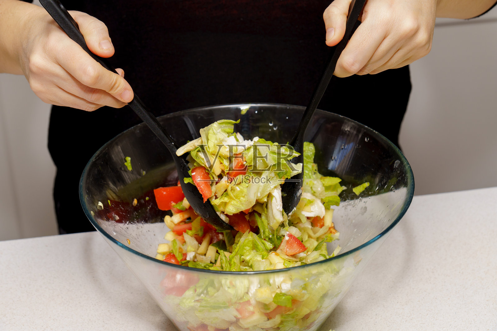 双手将新鲜健康的沙拉放入玻璃碗中照片摄影图片