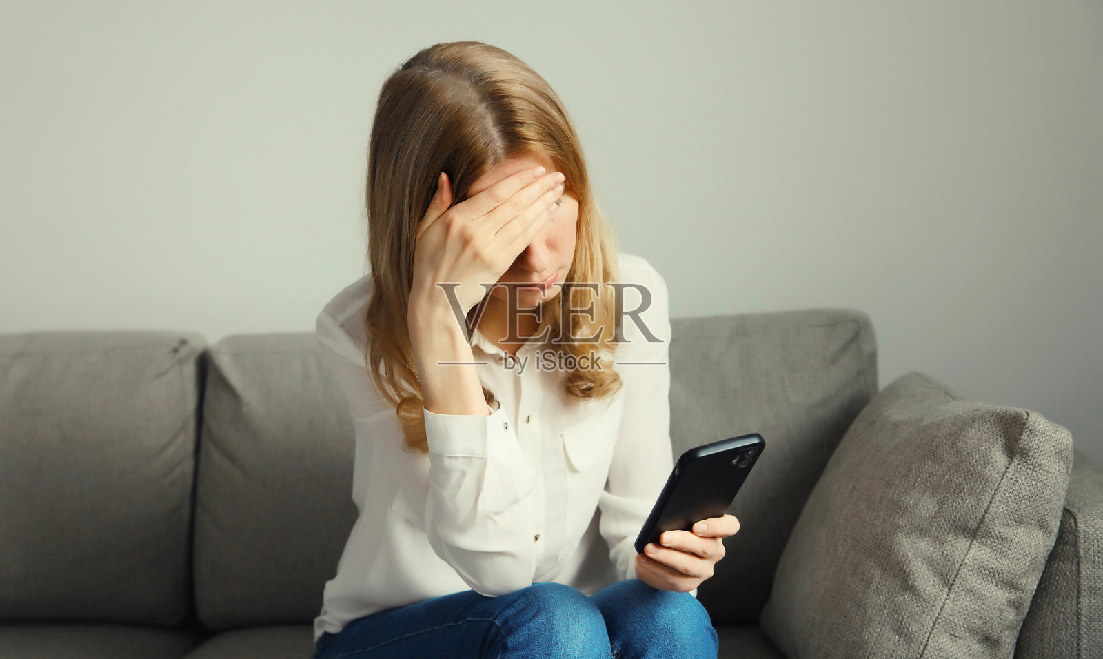 一名女子在家中因阅读了煽情信息而感到悲伤、沮丧、哭泣，承受着压力，手中拿着手机。照片摄影图片