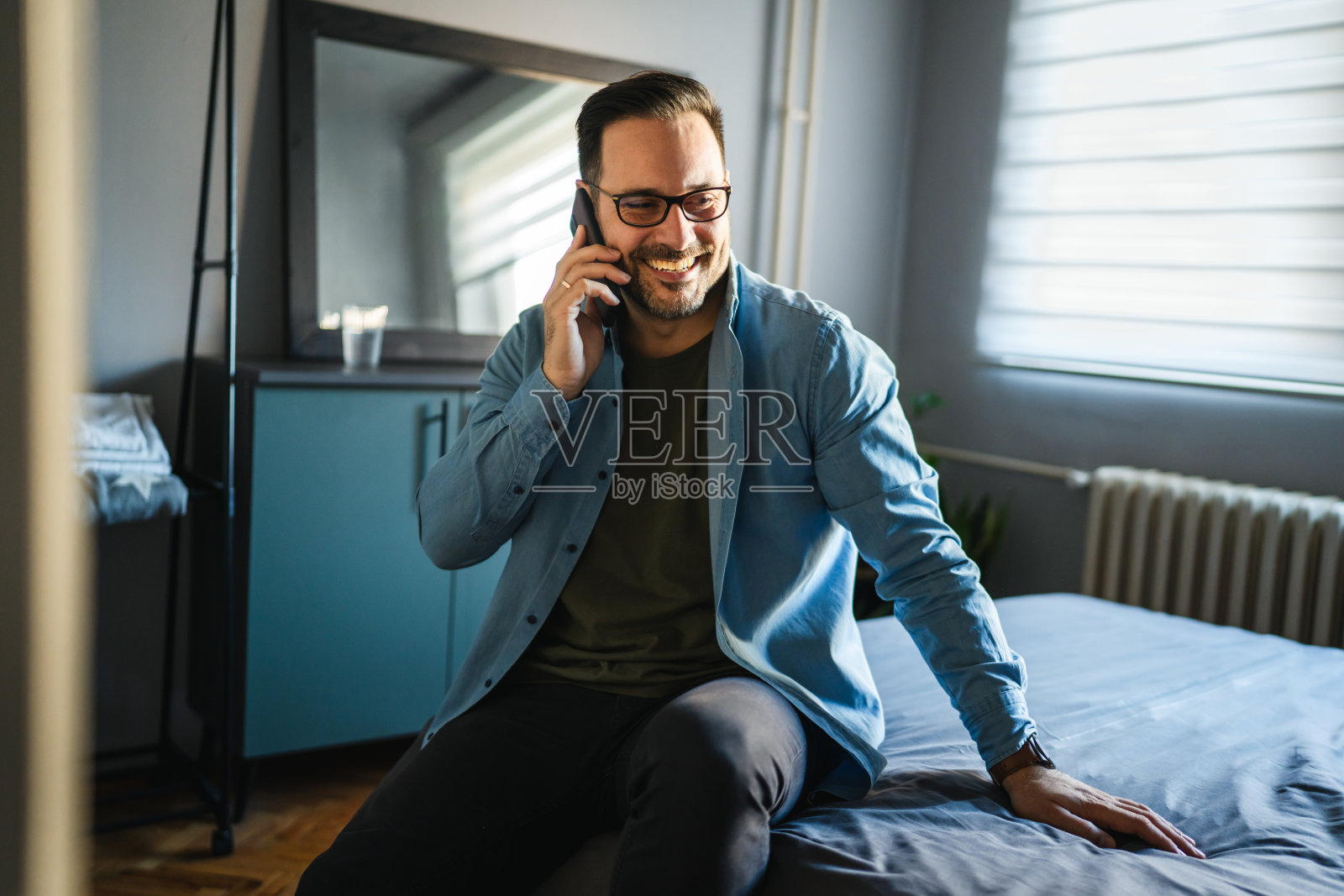 微笑的男人坐在床上用手机交流照片摄影图片