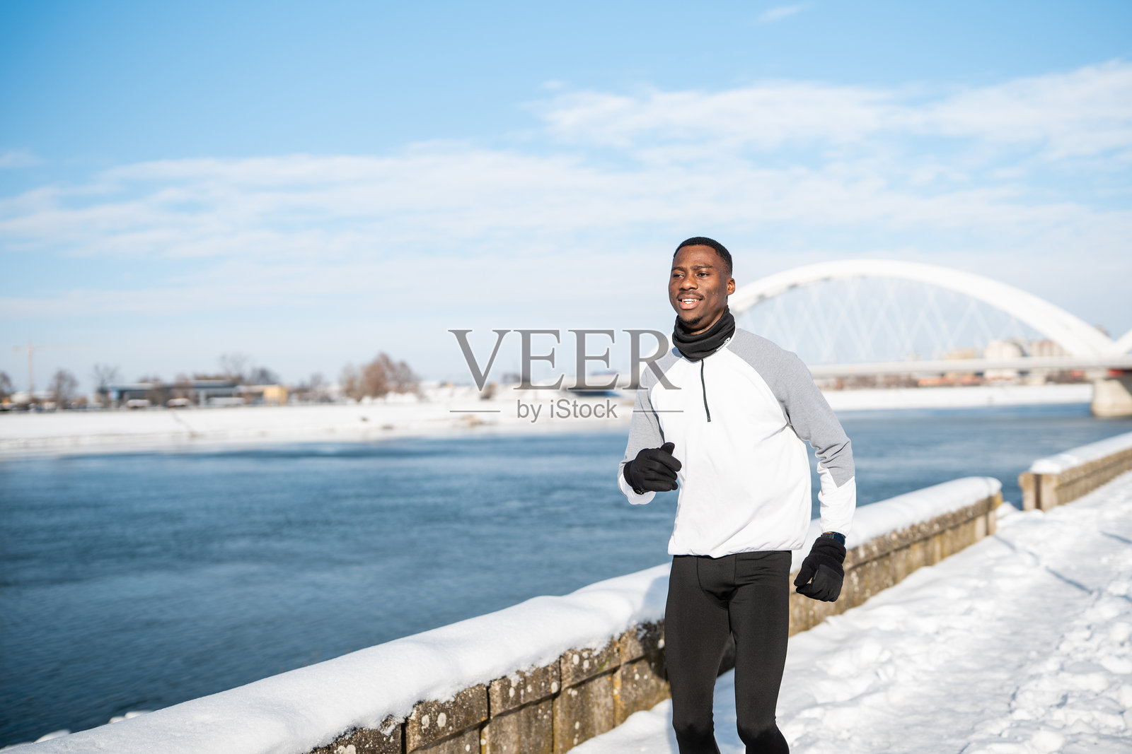 冬季，一名年轻的黑人男子在雪河边奔跑照片摄影图片