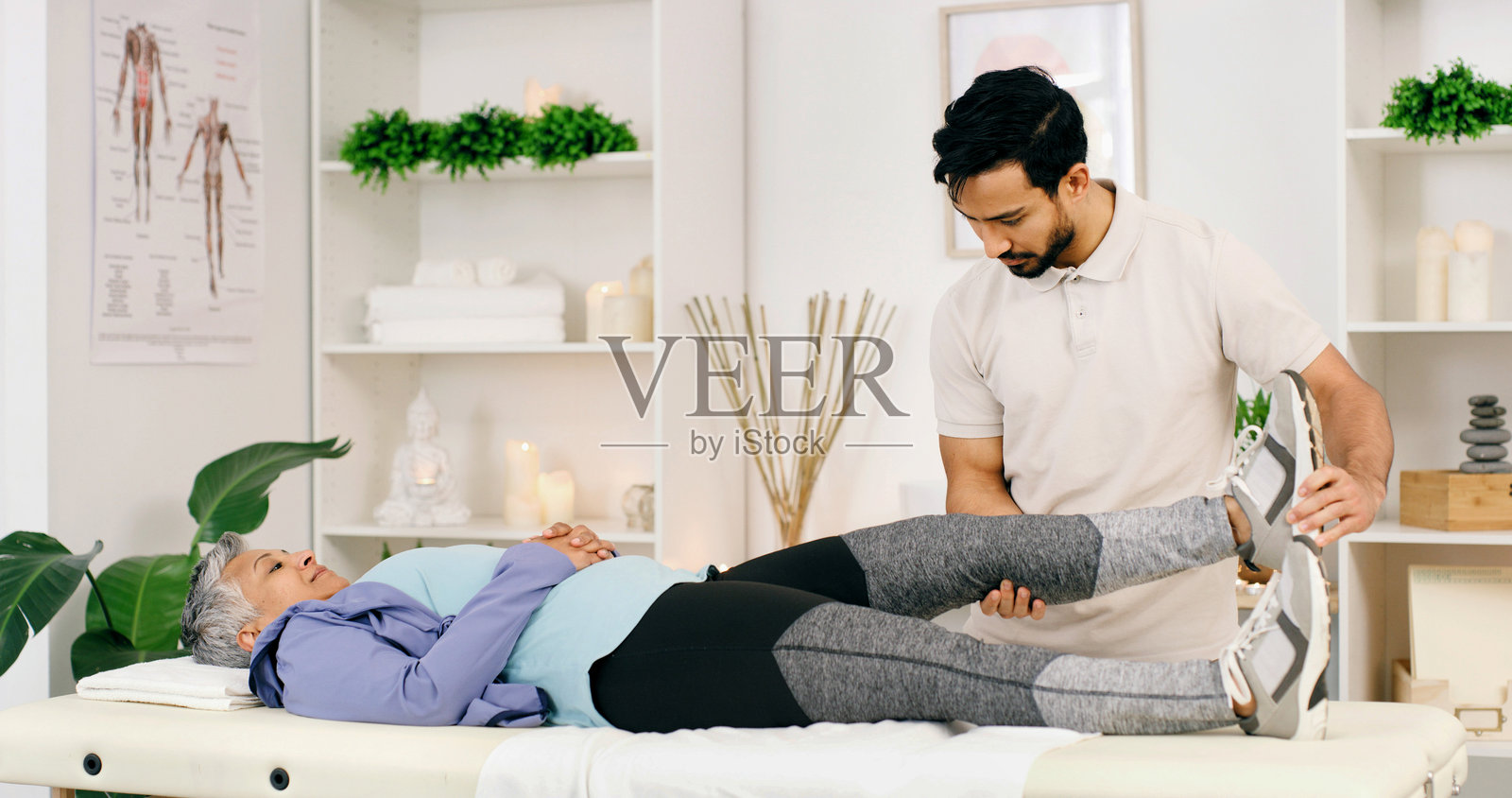 脊骨神经科医生在诊所为一位老年女性治疗腿部疼痛，帮助其肌肉恢复。医疗保健、体检和物理治疗师指导老年患者进行康复锻炼服务。照片摄影图片