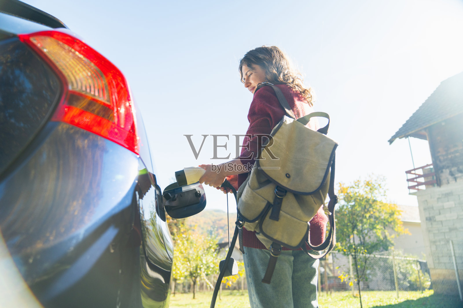 背着背包的女性旅行者站在充电中的电动汽车旁照片摄影图片