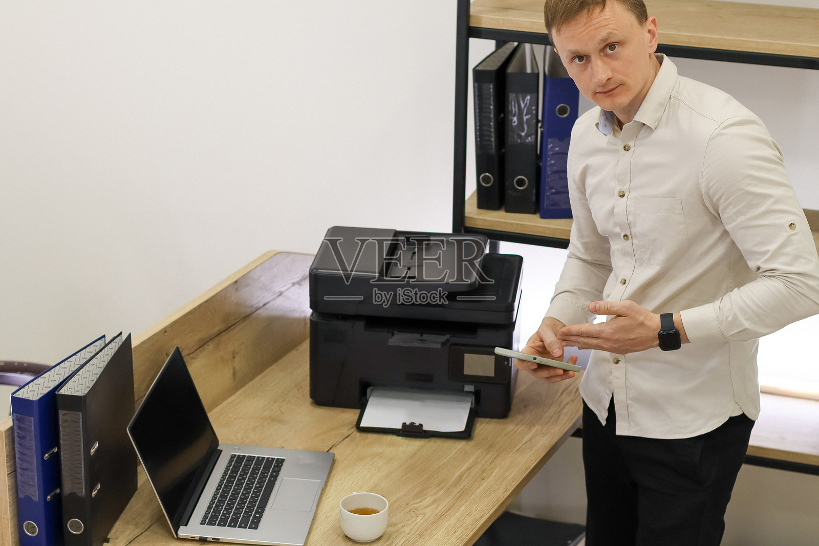 一名男子站在办公室打印机旁，用手指着手机照片摄影图片