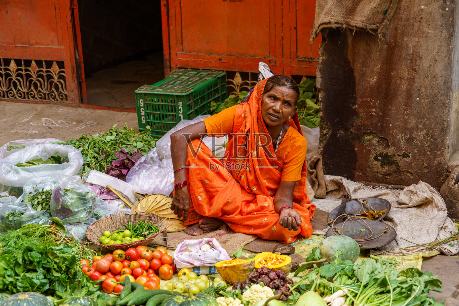 印度。北方邦。瓦拉纳西（贝拿勒斯）。一位蔬菜摊贩坐在她临时搭建的摊位后面，在街上售卖新鲜的水果和蔬菜照片摄影图片