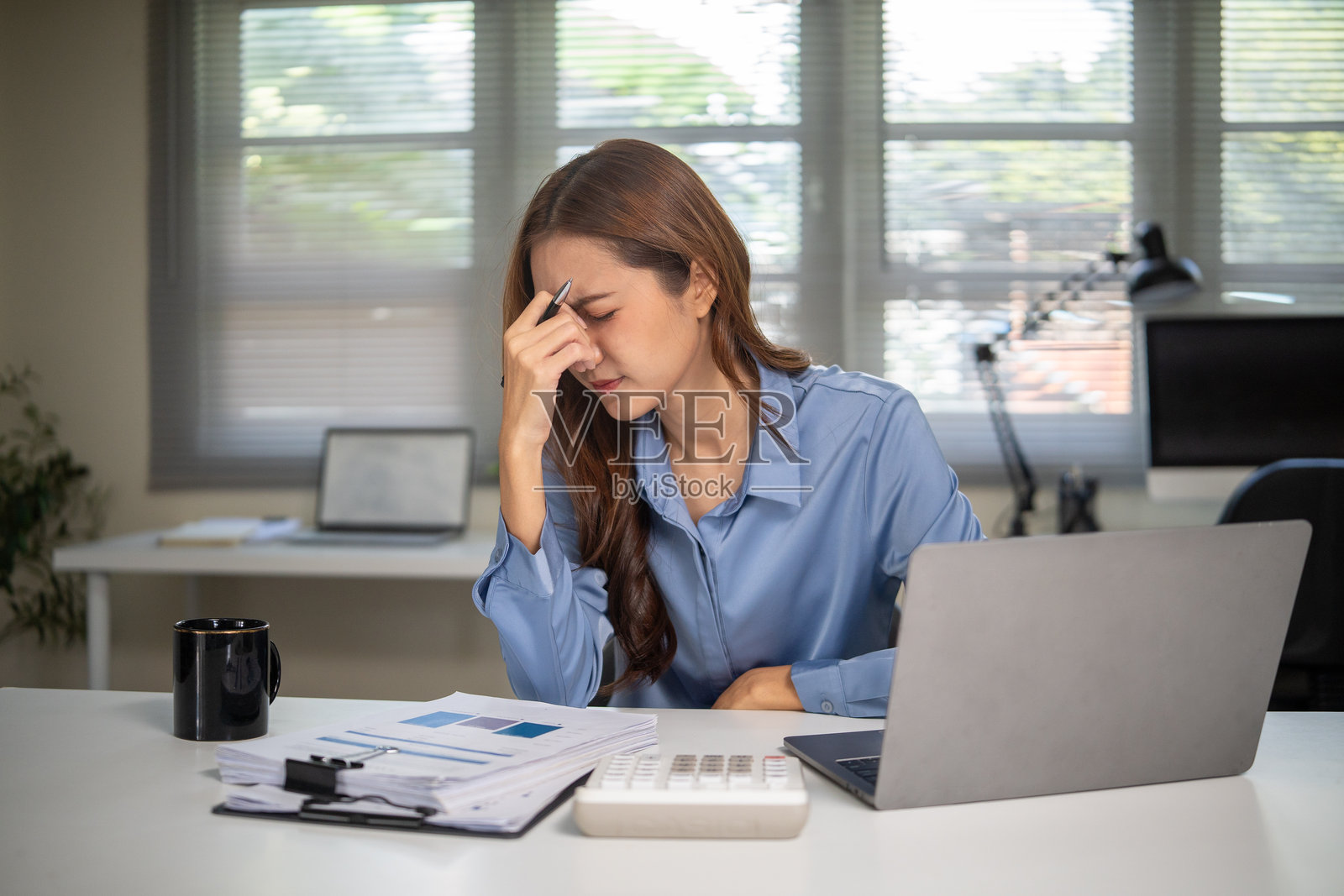 一位压力巨大的女商人在办公室办公桌前用笔记本电脑工作，双手抱头，体现了职场压力和截止日期的概念。照片摄影图片