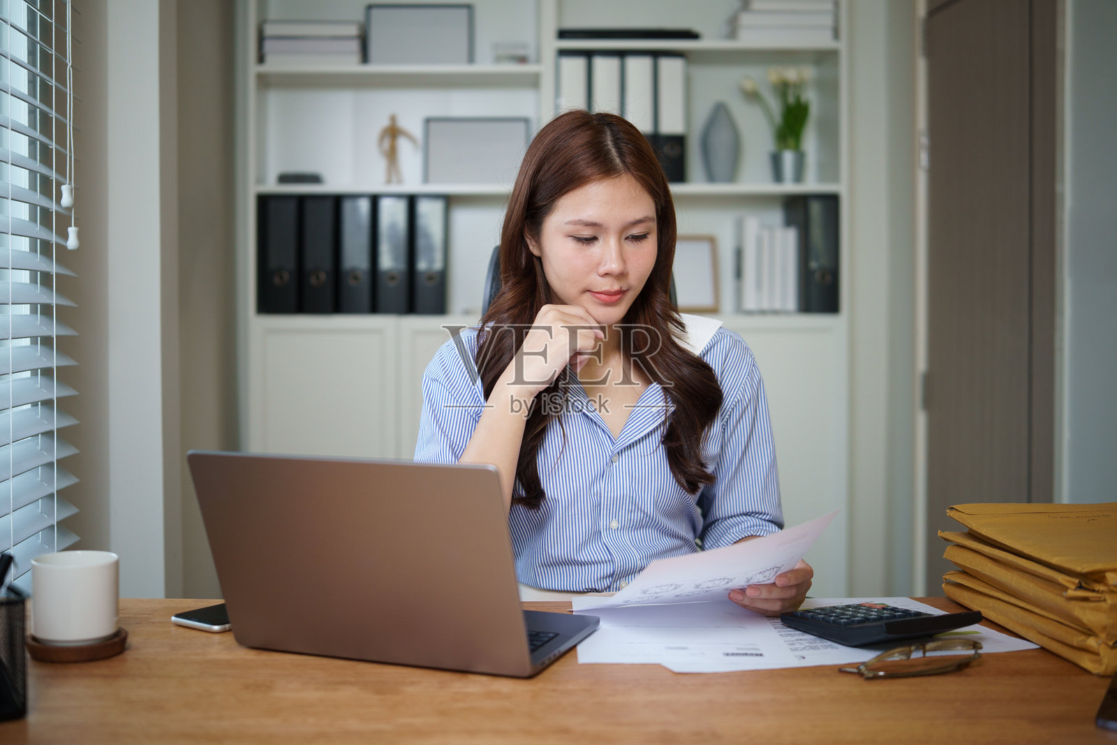 女商人坐在办公室的桌子旁，使用笔记本电脑分析文件，象征着财务与管理的概念。照片摄影图片