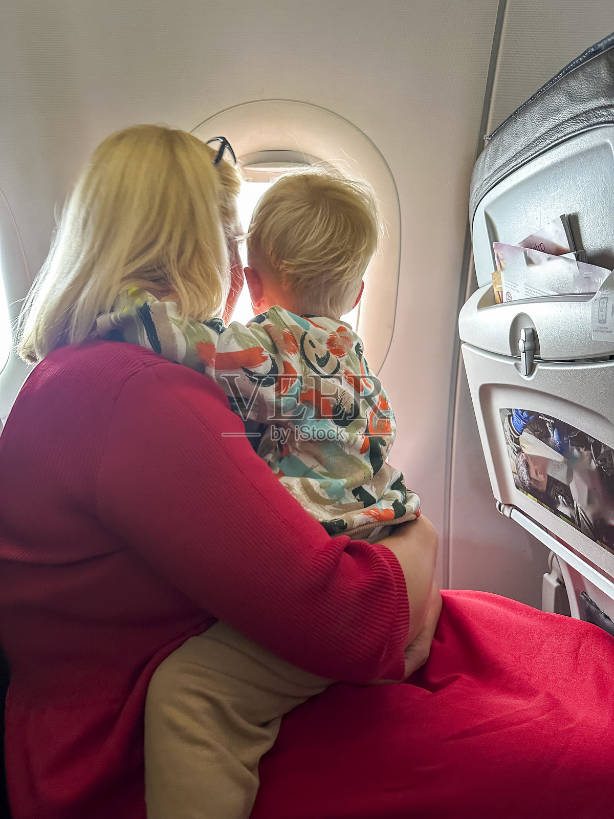 年轻的白人孩子在飞机旅途中拥抱母亲照片摄影图片