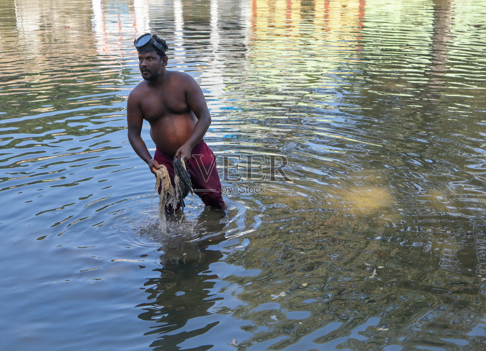 印度卡纳塔克邦，一名市政工人正在污染的河水中收集垃圾、塑料、衣物和淤泥，以进行废物管理和环境保护。照片摄影图片