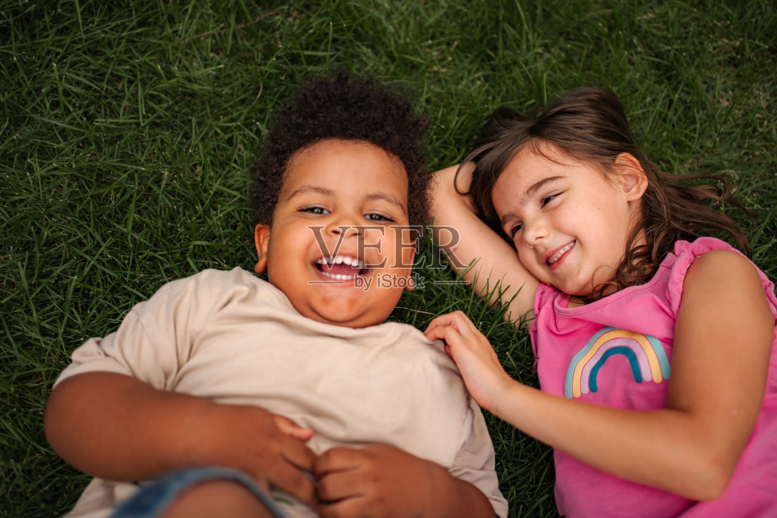 一群不同背景的孩子在户外绿草地上开怀大笑，尽情玩耍。照片摄影图片