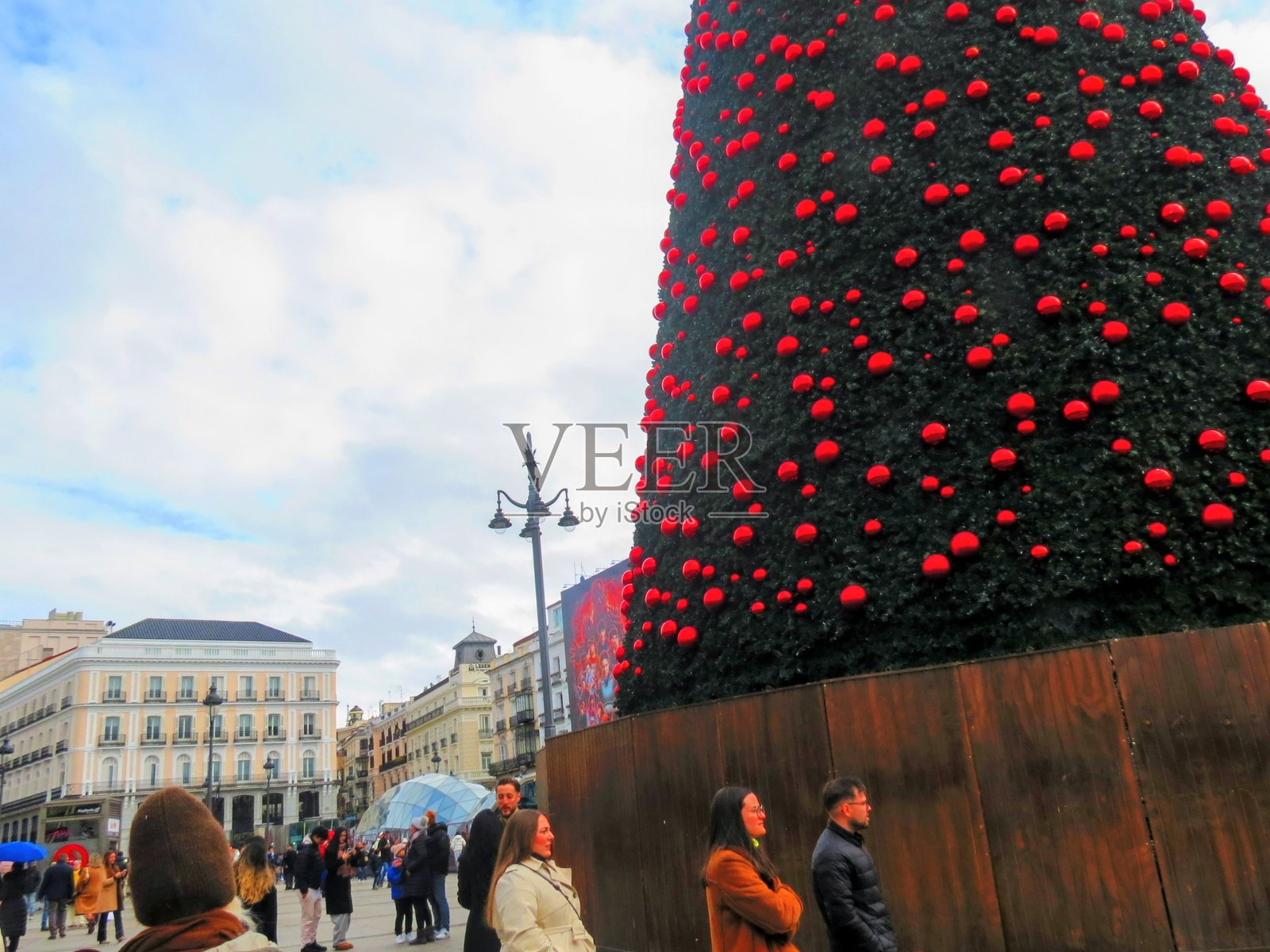 马德里太阳门广场上，喜庆的人群聚集在一棵巨大的圣诞树周围。照片摄影图片