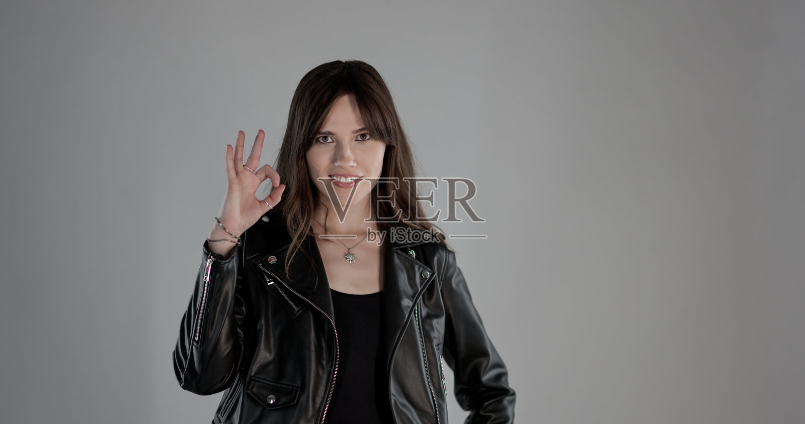 身穿皮夹克的年轻女子竖起“OK”手势，面带微笑照片摄影图片