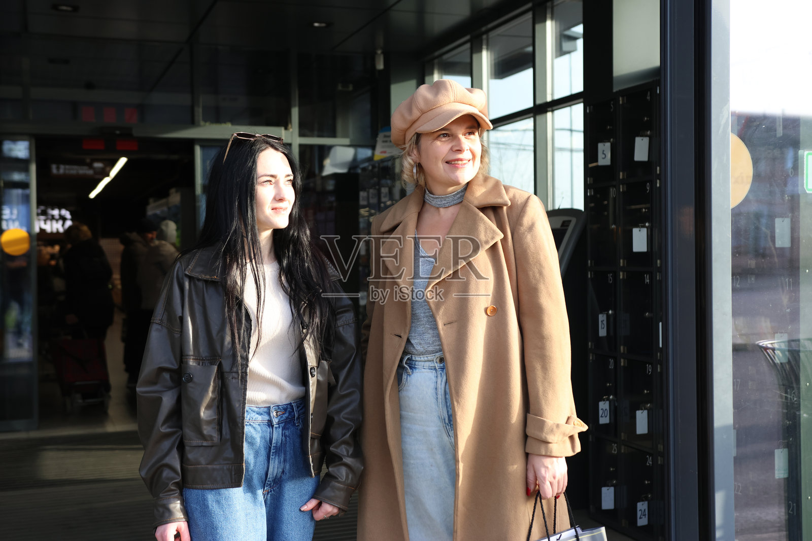 两位女士在购物后，于晴朗的一天站在购物中心附近，看向一旁。照片摄影图片